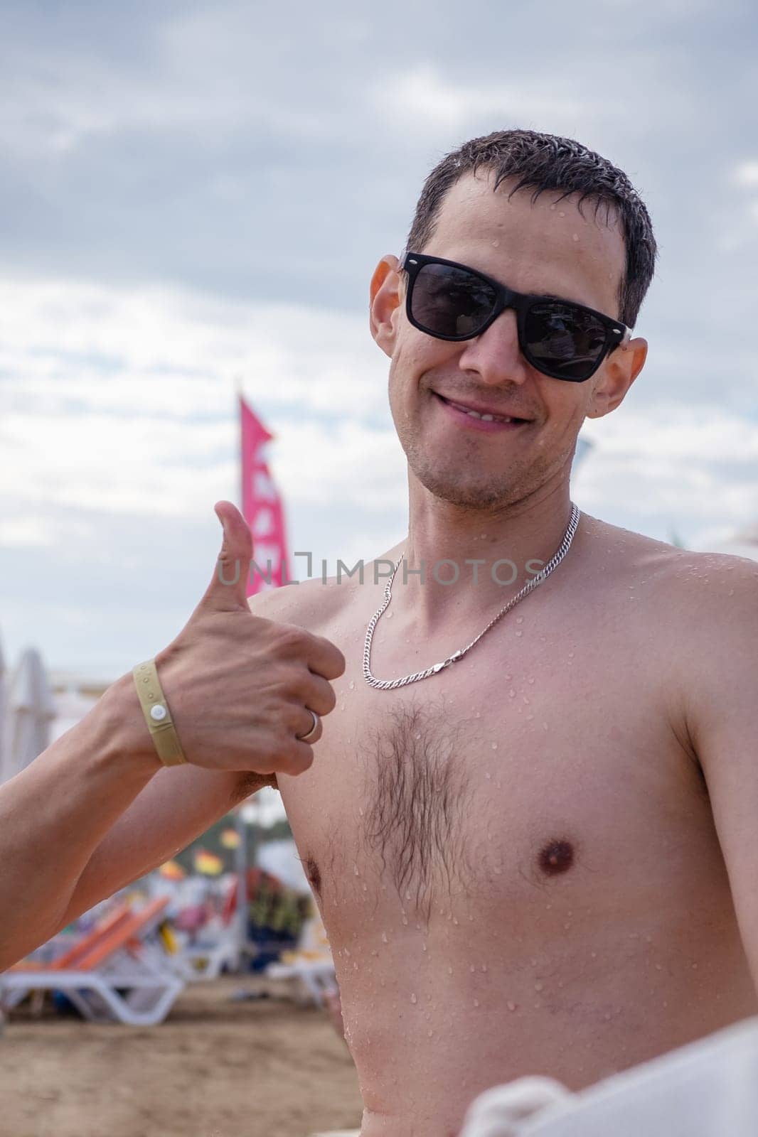Close-up portrait of a man in black glasses at sea. The man shows his thumbs up. Handsome man on vacation looking at camera.