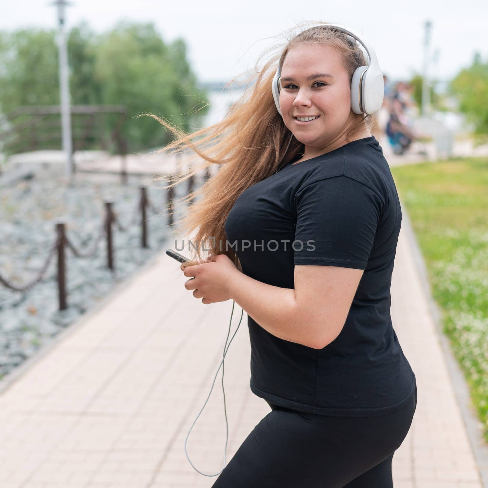 Young fat woman in headphones walks outdoors and listens to music on a smartphone by mrwed54