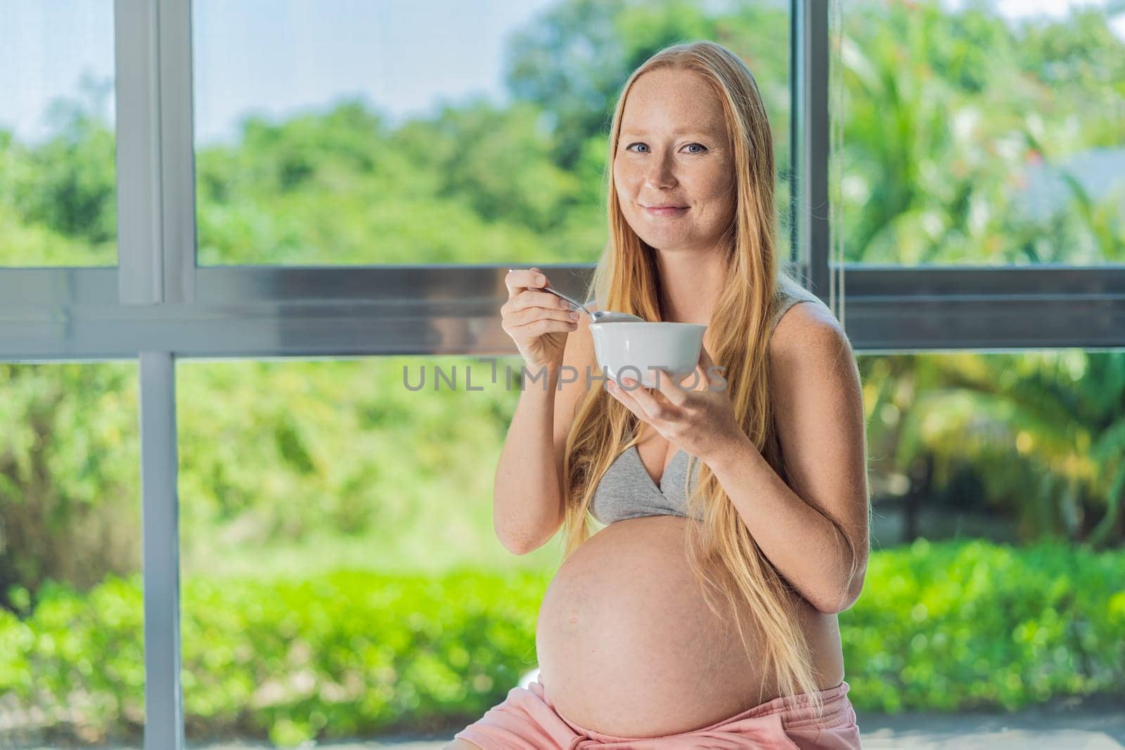 An expecting mother gracefully has breakfast on a fitness ball, illustrating the comfort it provides during pregnancy when traditional chairs may be less accommodating by galitskaya