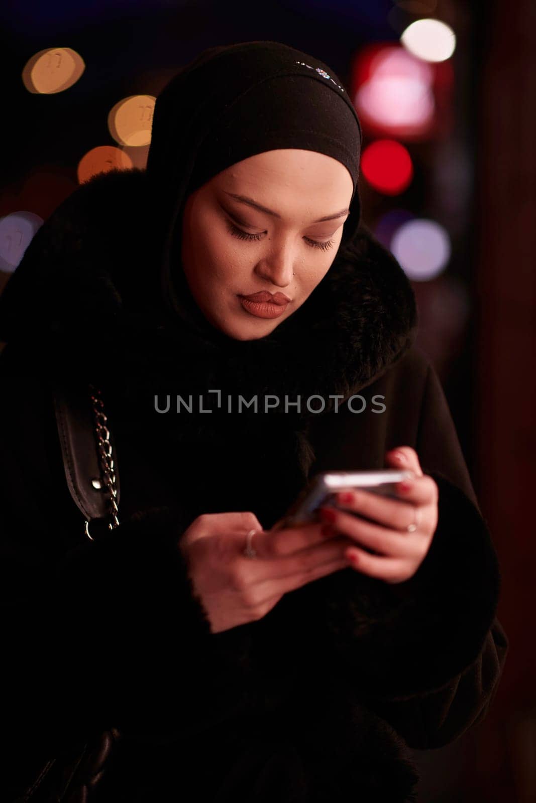 uropean Muslim Hijabi Business Lady checking her phone on urban city street at night by dotshock