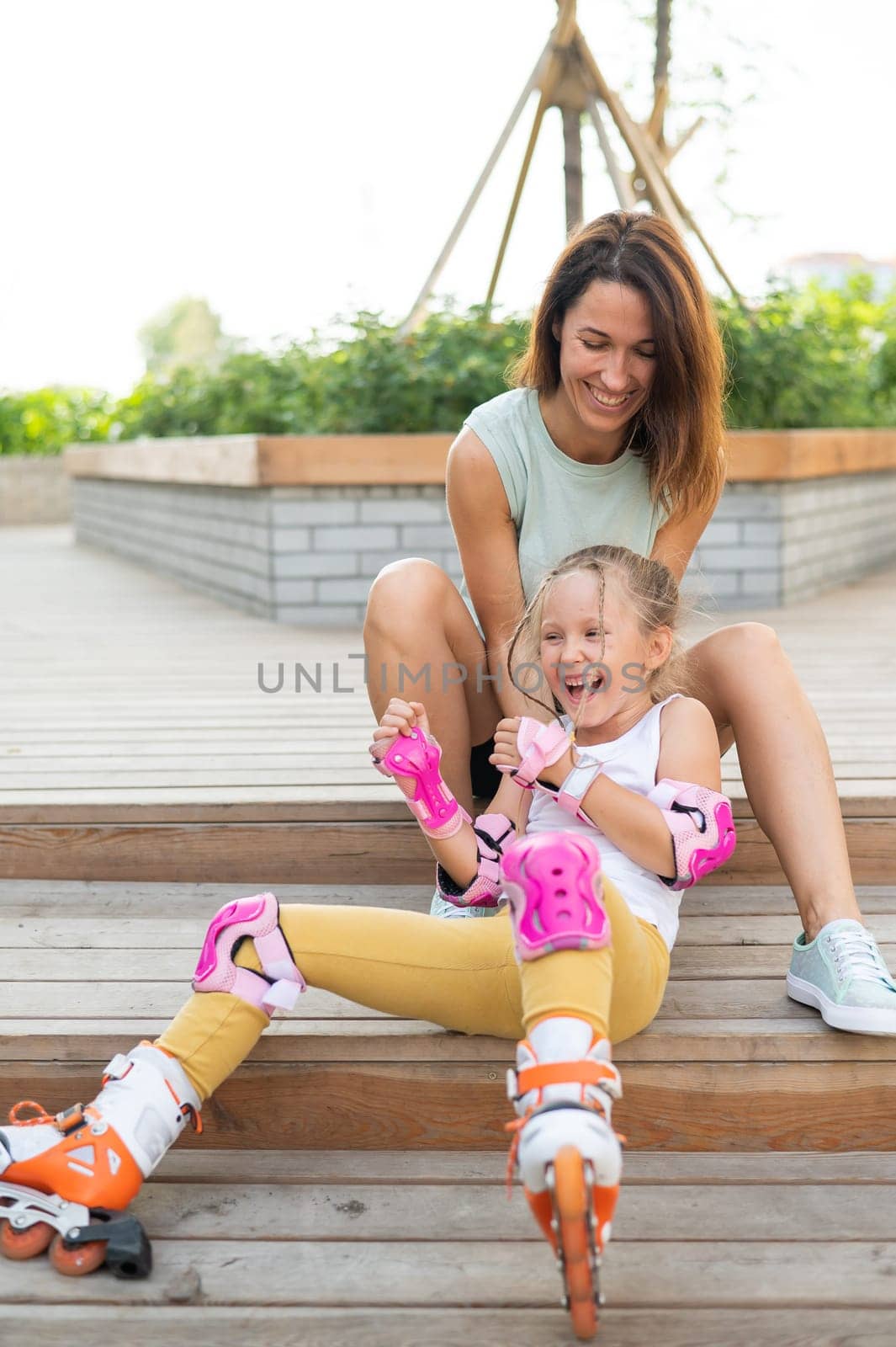 Little girl in roller skates and her mom sit on a wooden ladder and hug outdoors