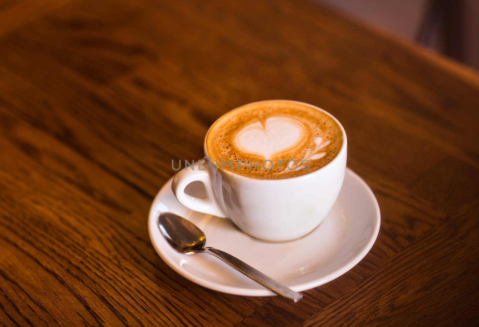 A cup of coffee with heart pattern in a white cup on wooden background