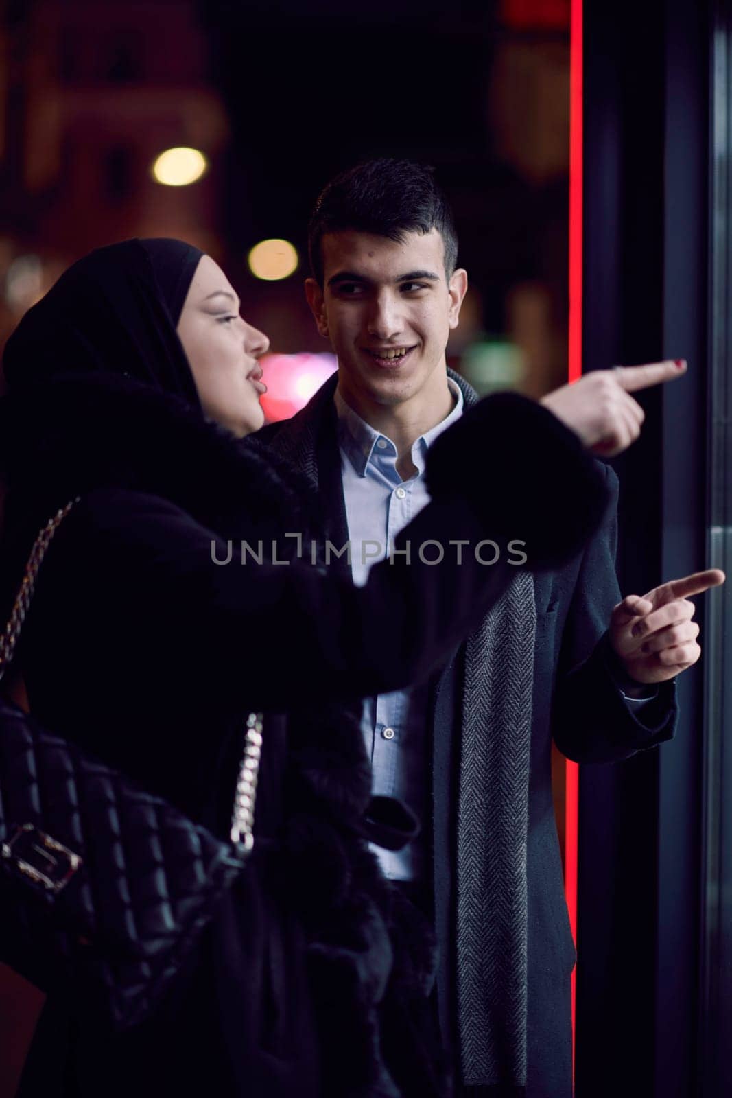Happy multicultural business couple walking together outdoors in an urban city street at night near a jewelry shopping store window. by dotshock