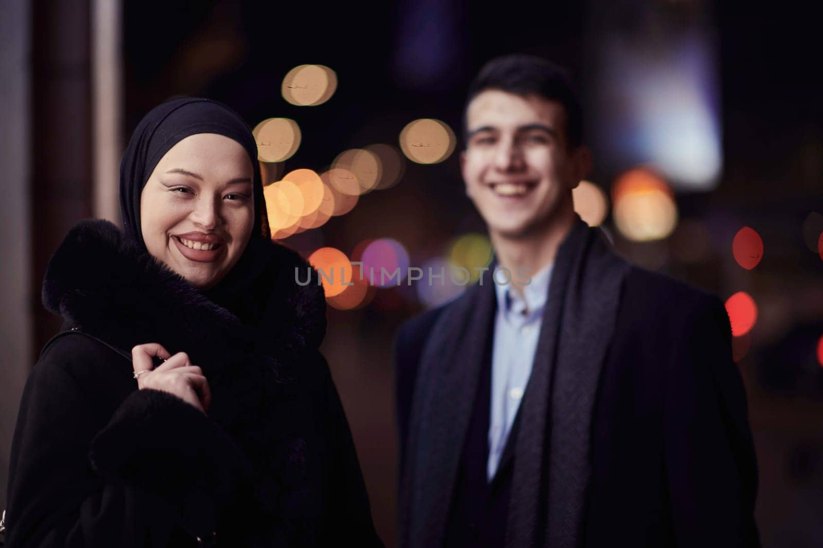 Happy multicultural business couple walking together outdoors in an urban city street at night near a jewelry shopping store window. by dotshock