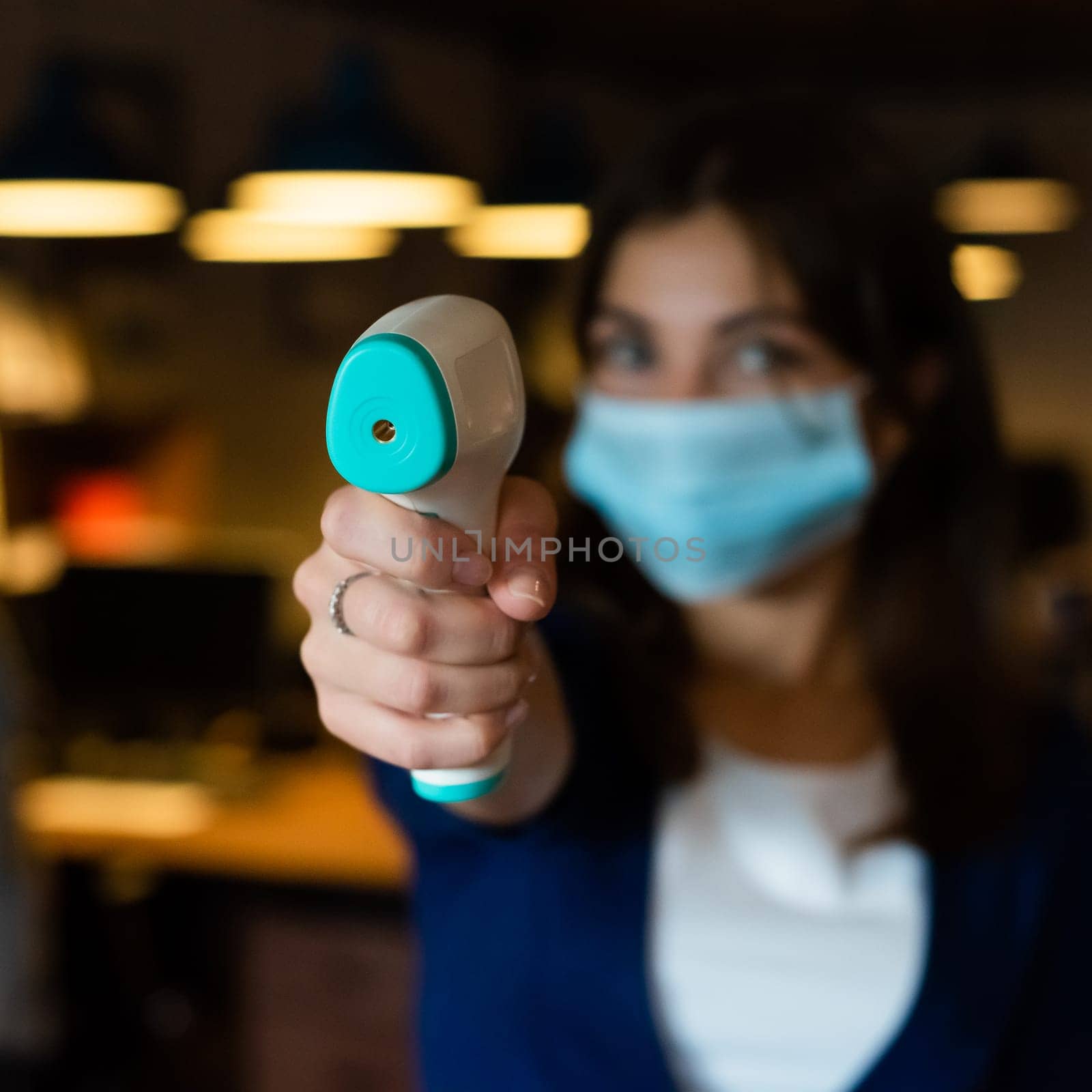 A female office worker in a mask holds a contactless electronic thermometer.