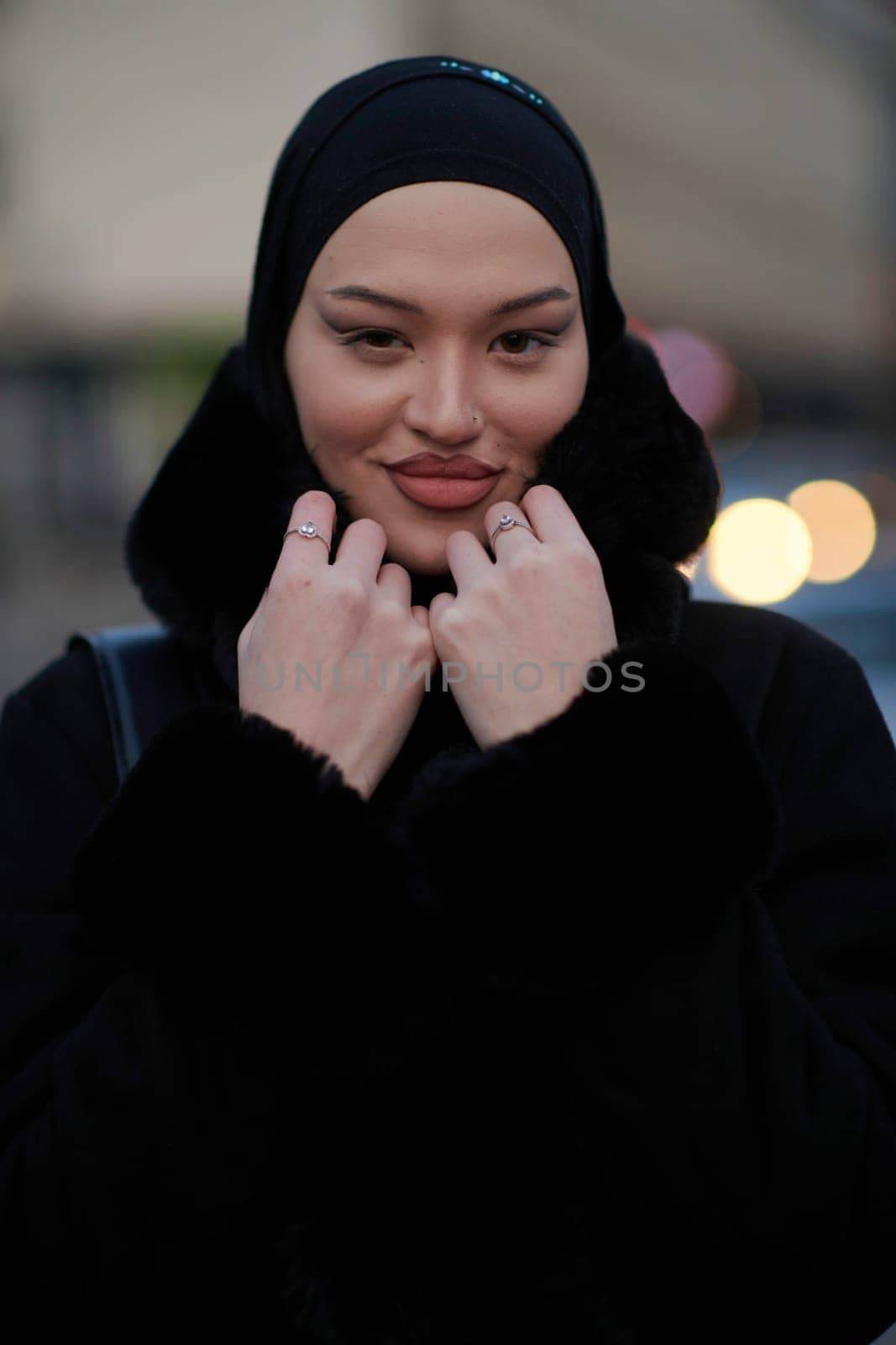 Muslim woman walking on an urban city street on a cold winter night wearing hijab with bokeh city lights in the background