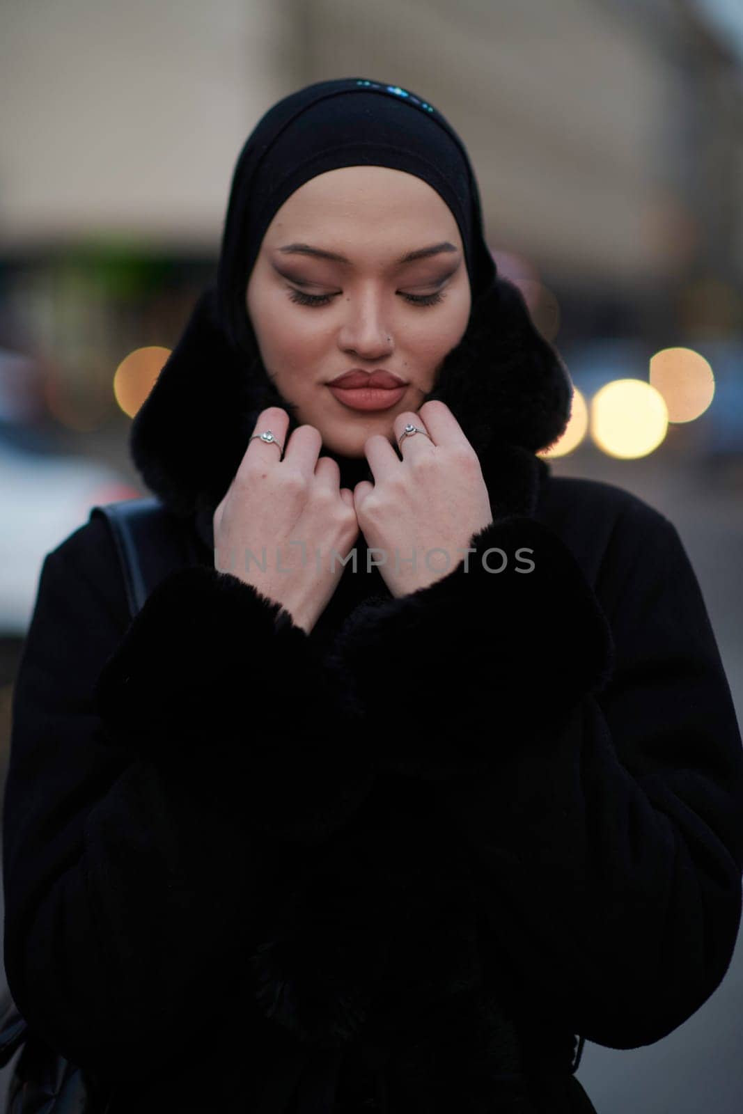 Muslim woman walking on an urban city street on a cold winter night wearing hijab with bokeh city lights in the background