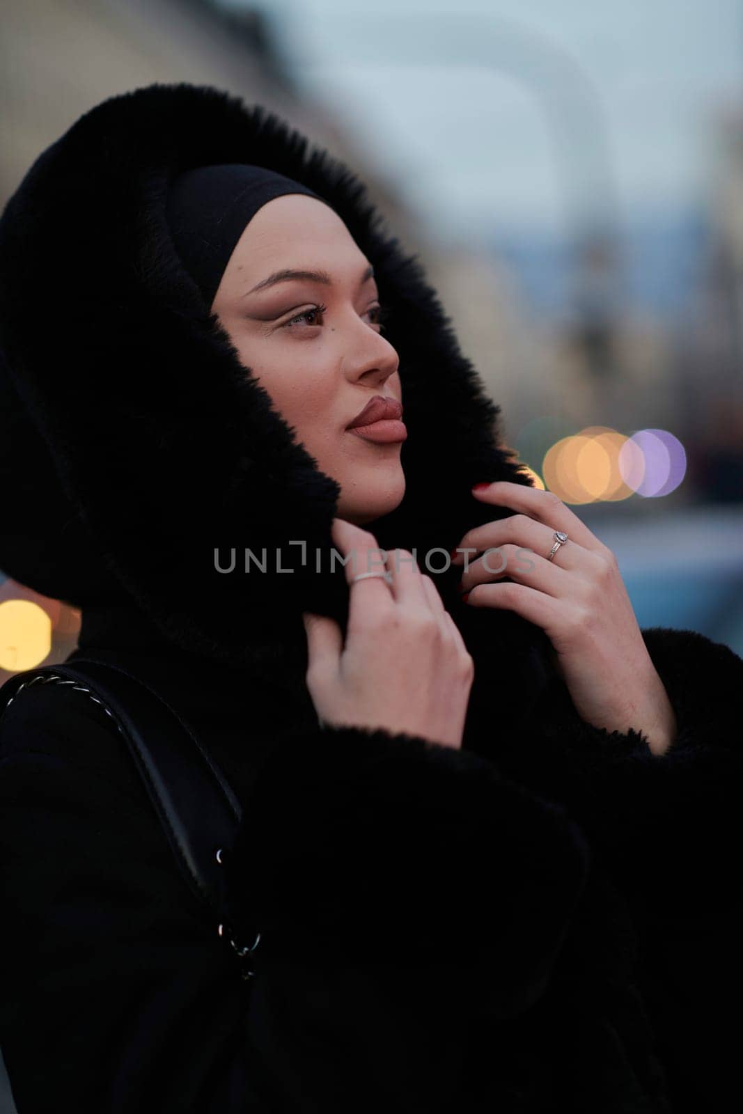 Muslim woman walking on an urban city street on a cold winter night wearing hijab with bokeh city lights in the background