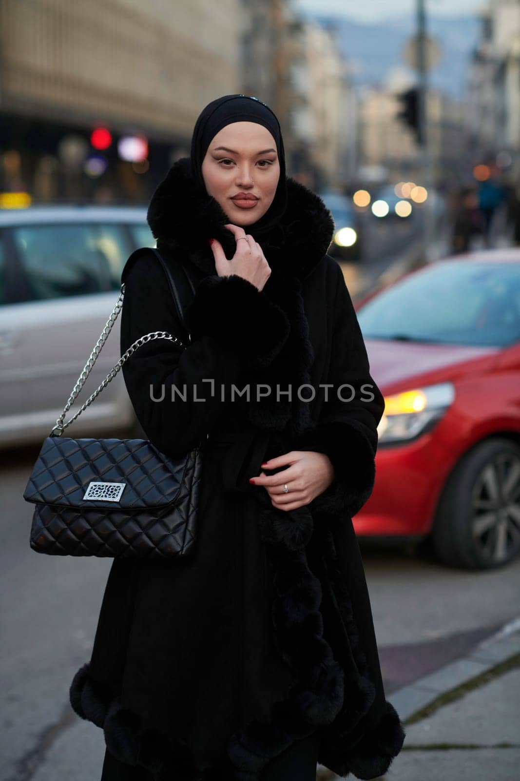 Muslim woman walking on an urban city street on a cold winter night wearing hijab with bokeh city lights in the background