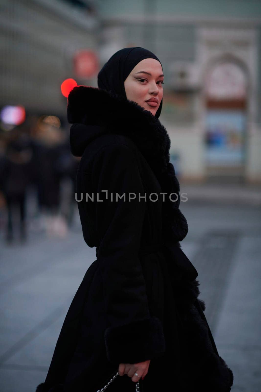 Muslim woman walking on an urban city street on a cold winter night wearing hijab with bokeh city lights in the background