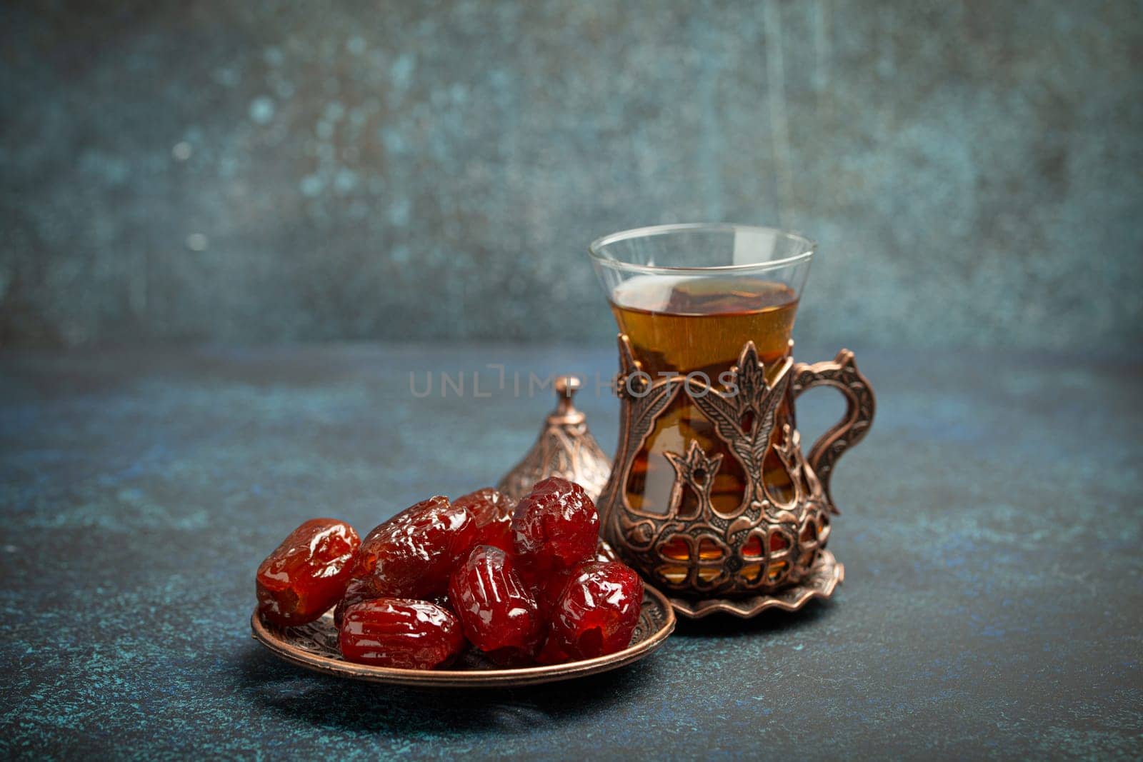 Breaking fasting with dried dates during Ramadan Kareem, Iftar meal with dates and Arab tea in traditional glass, angle view on rustic blue background. Muslim feast by its_al_dente