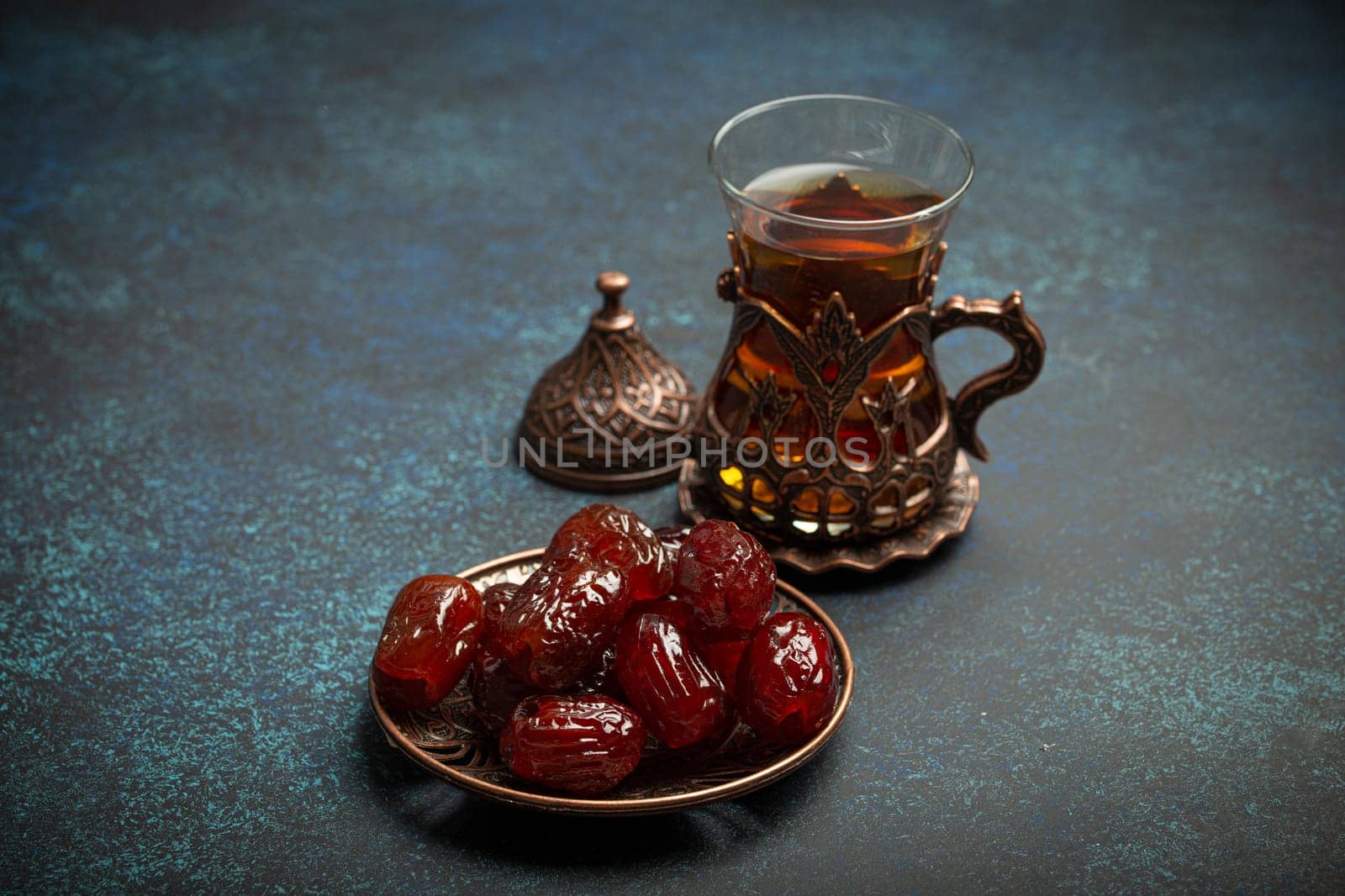 Breaking fasting with dried dates during Ramadan Kareem, Iftar meal with dates and Arab tea in traditional glass, angle view on rustic blue background. Muslim feast by its_al_dente