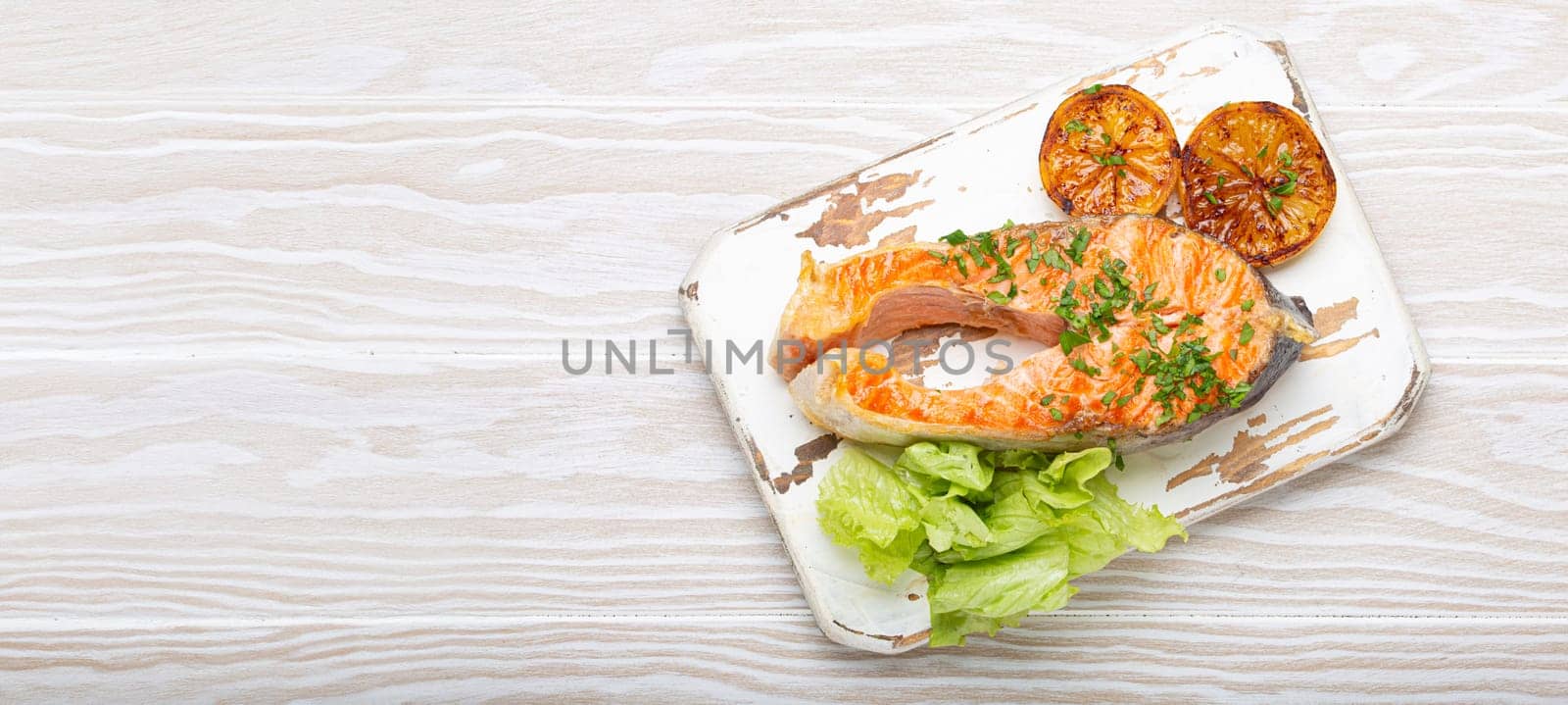 Grilled fish salmon steak and green salad with lemon served on white cutting board rustic wooden background top view, balanced diet or healthy nutrition meal with salmon and veggies, copy space.