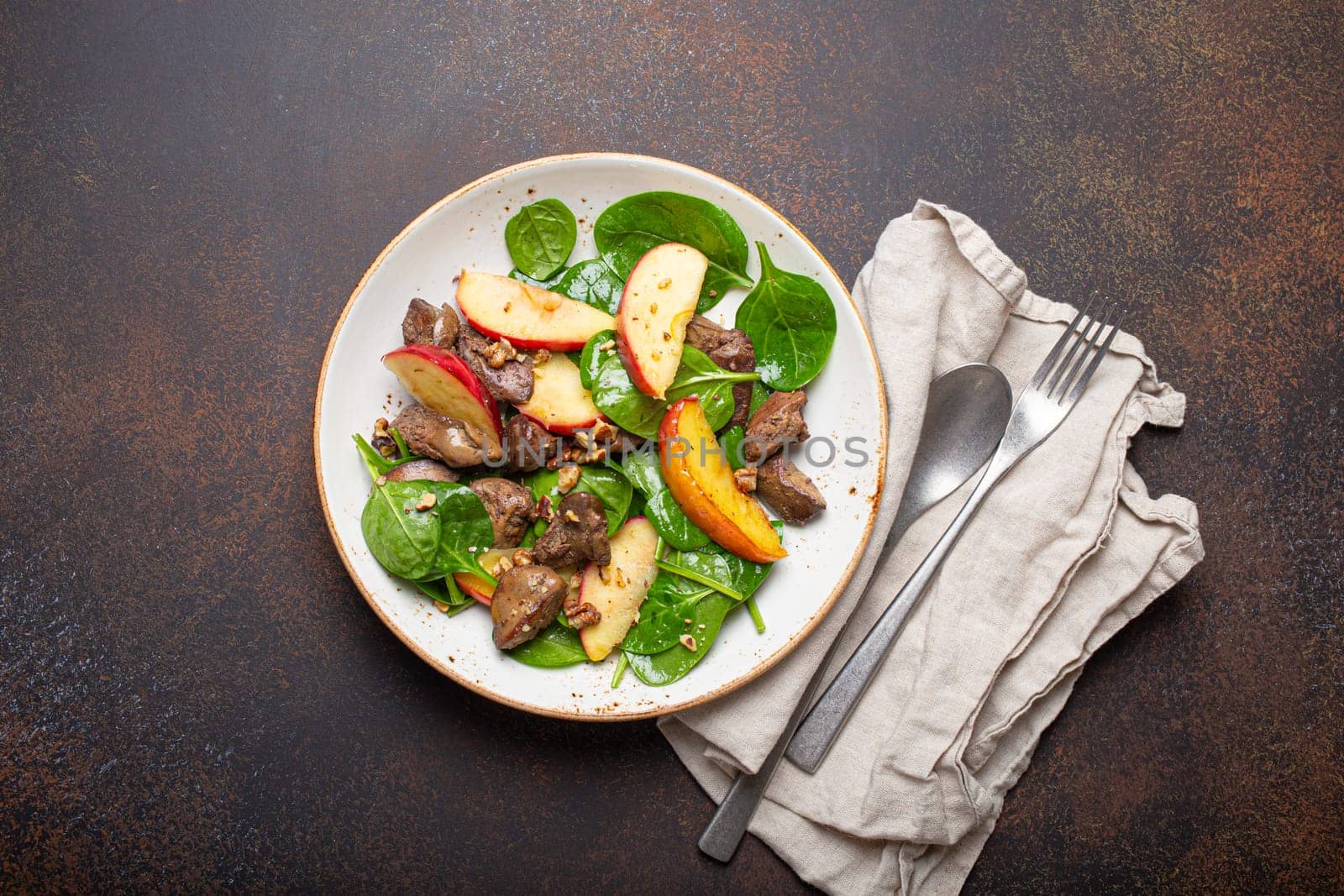 Healthy Salad with Iron Rich Ingredients Chicken Liver, Apples, Fresh Spinach and Walnuts on White Ceramic Plate, Dark Brown Rustic Stone Background From Above. by its_al_dente