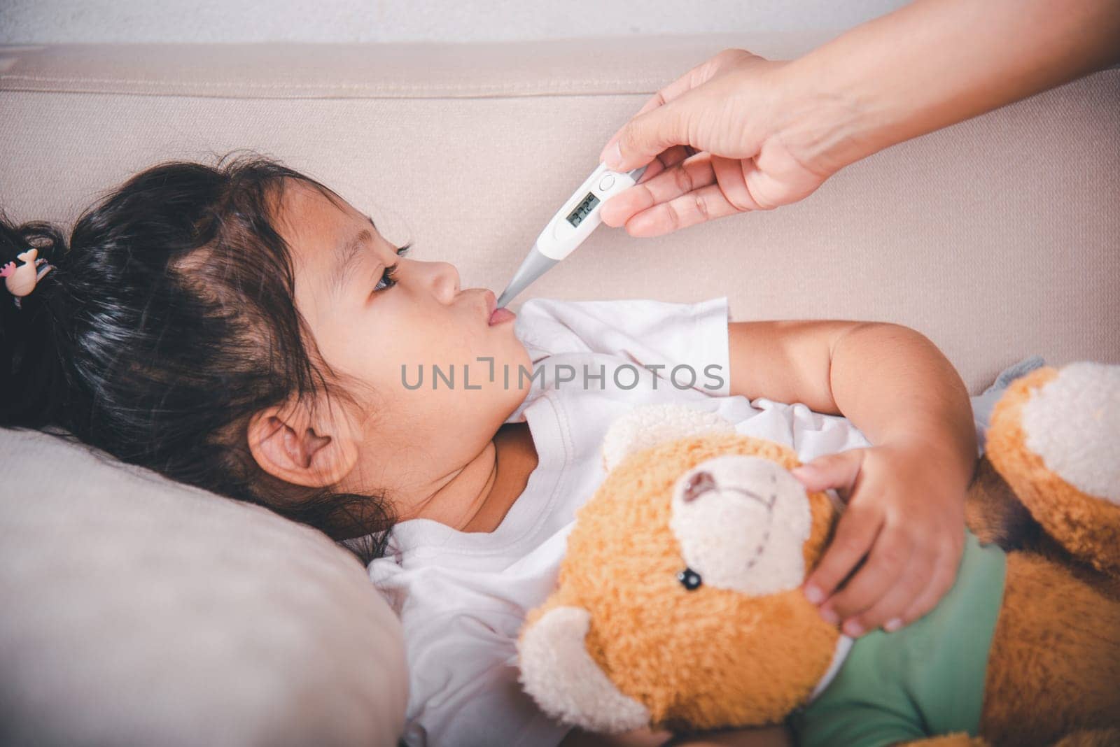 Mother parent checking temperature of her sick daughter with digital thermometer in mouth by Sorapop