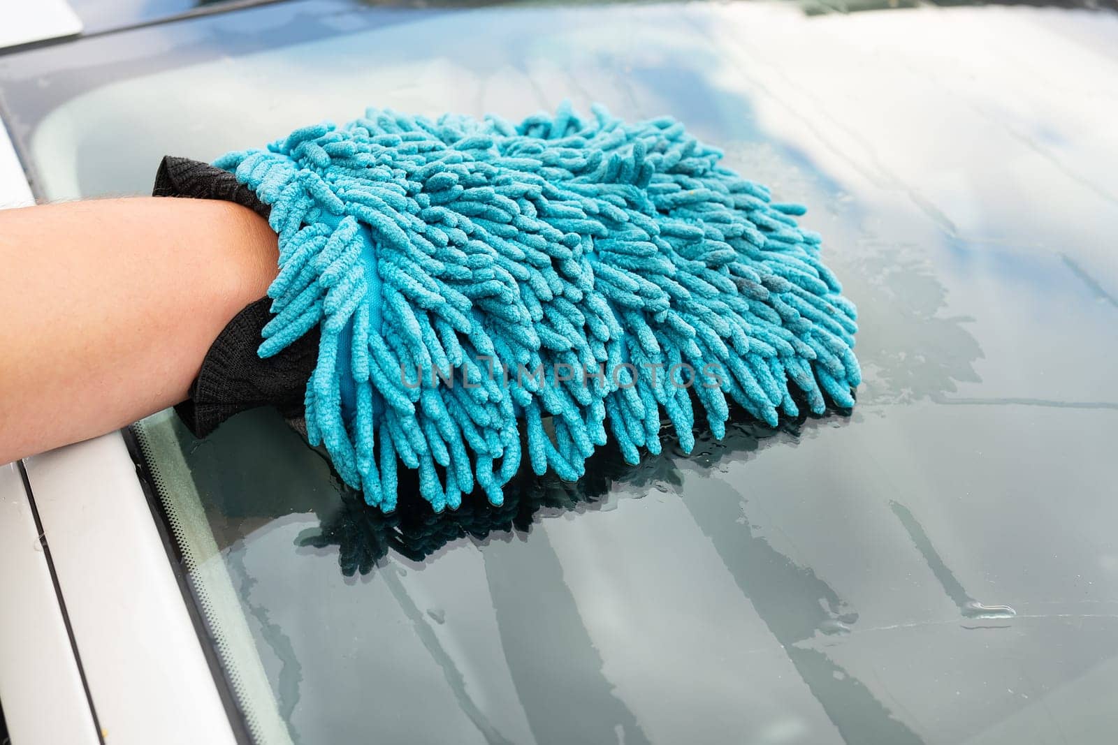 A man washes the car windshield with a large blue washcloth. Car wash, self-service