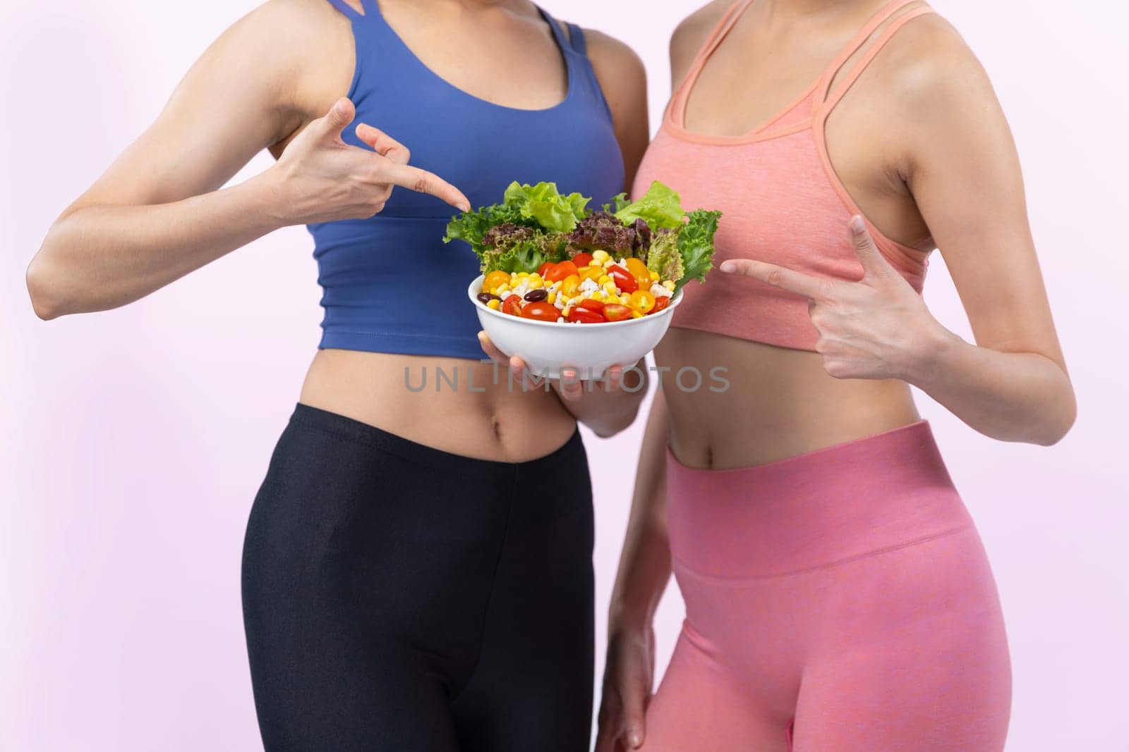 Two young sporty Asian women in sportswear holding salad bowl fill with fruit and vegetable. Natural youthful and fit body lifestyle people with balance nutrition on isolated background. Vigorous