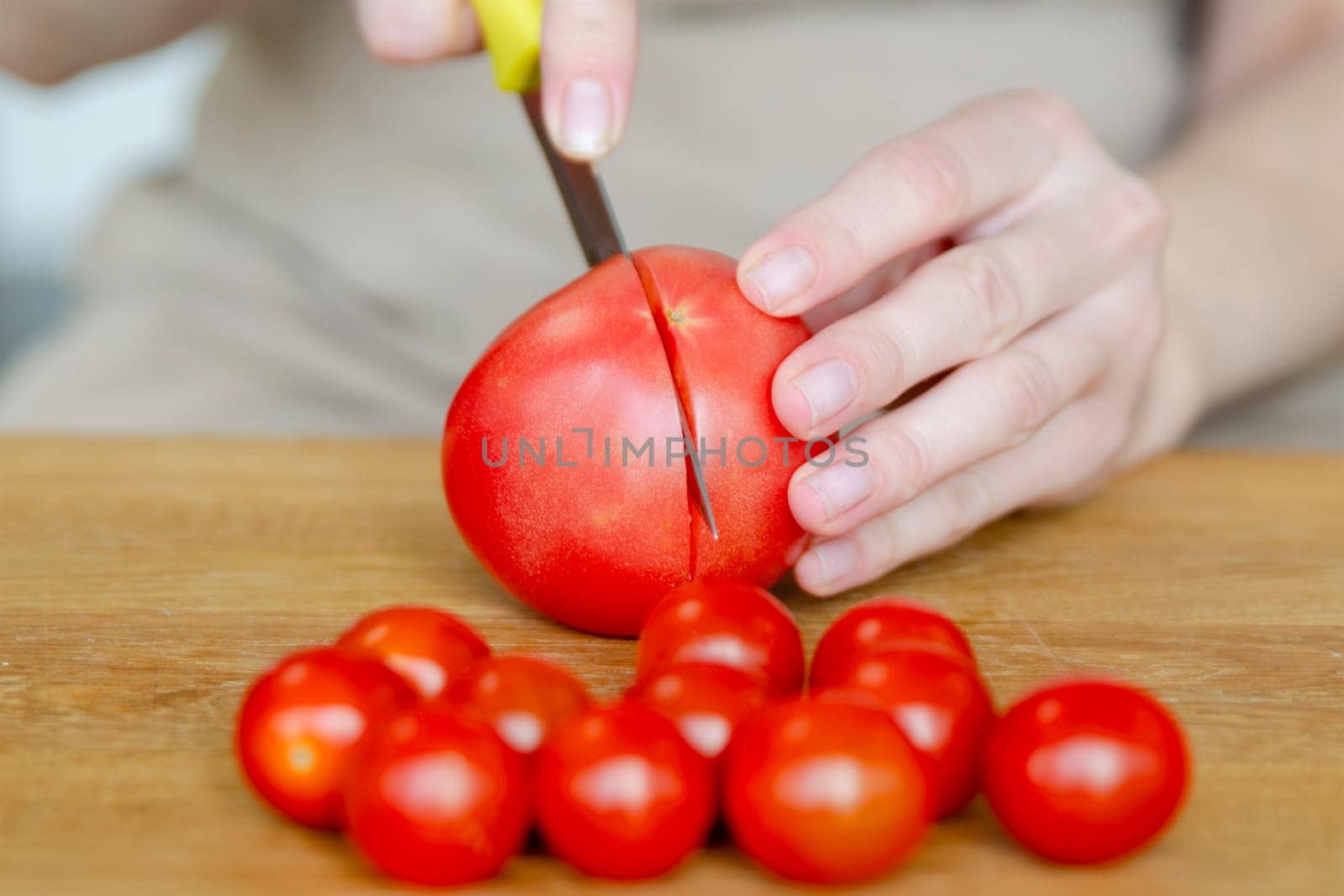 Preparing summer salad with tomatoes close-up. A woman's hands cut a tomato in half for a salad or side dish. High quality photo