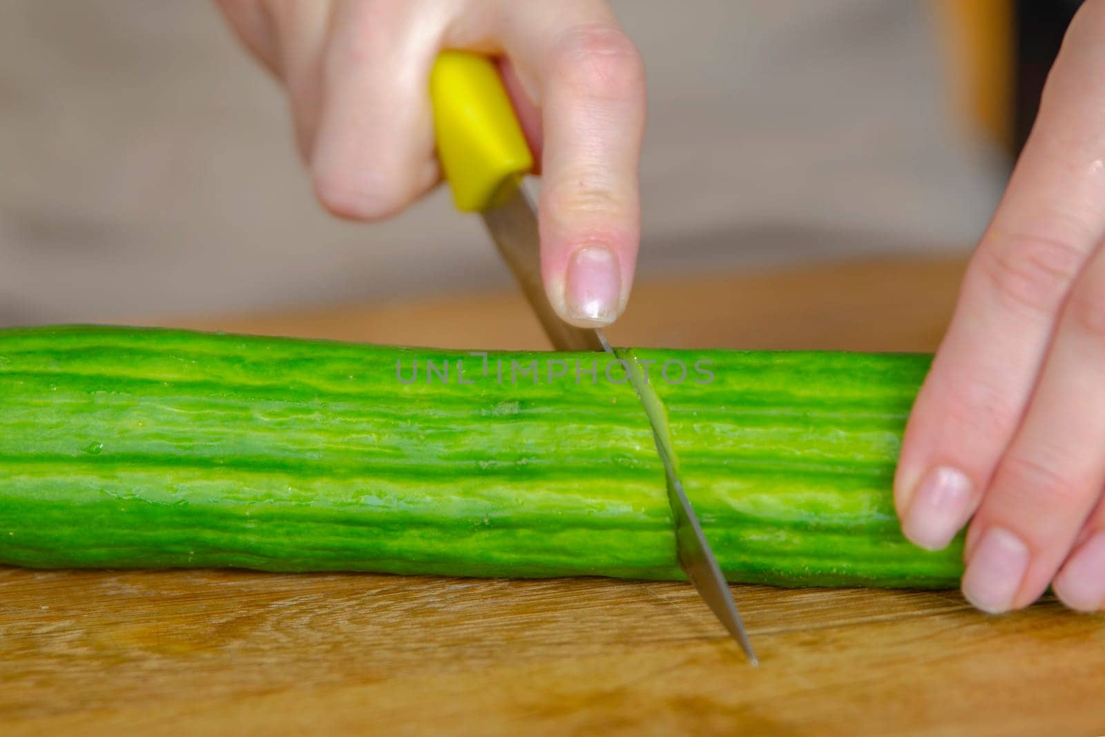 A woman's hands cut a green cucumber in half, close-up. Long green cucumber are suitable for salads or as a side dish. Preparing cucumbers for salad