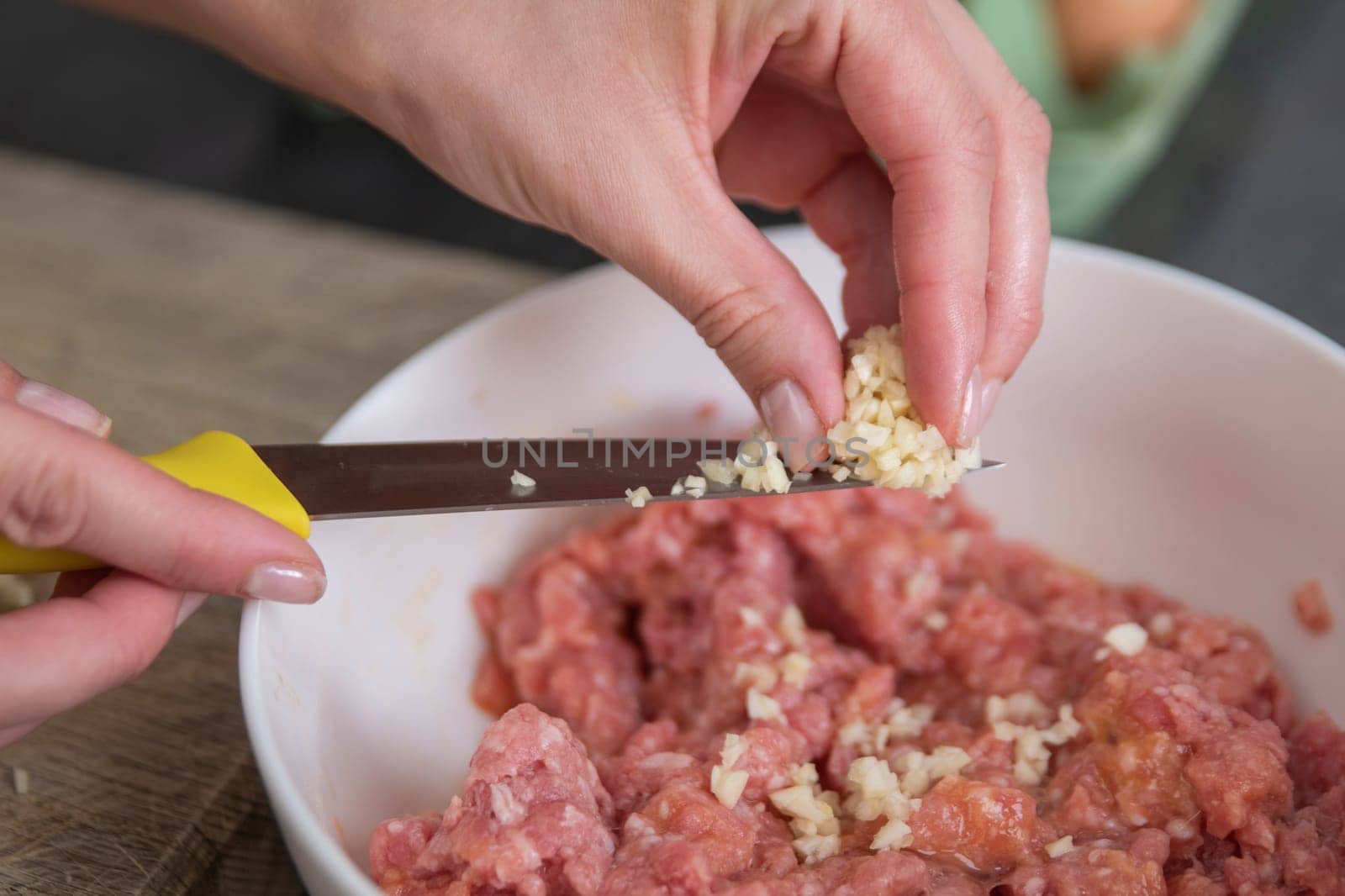 A woman's hand sprinkles finely chopped garlic into a raw chopped meat, close-up. Fresh garlic, diced, is used as a raw meat dressing