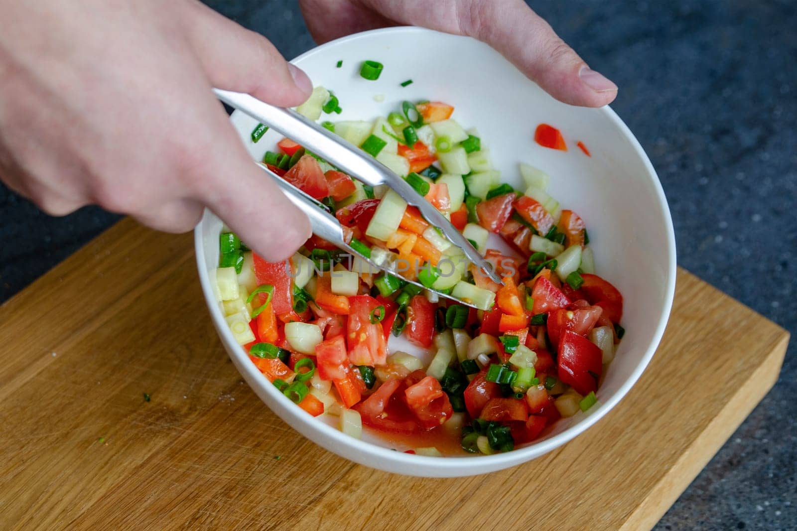 The process of mixing salad. Close-up of a man's hands stirring a salad mixture. Hands stir the salad so that the ingredients are distributed throughout the plate. by SERSOL