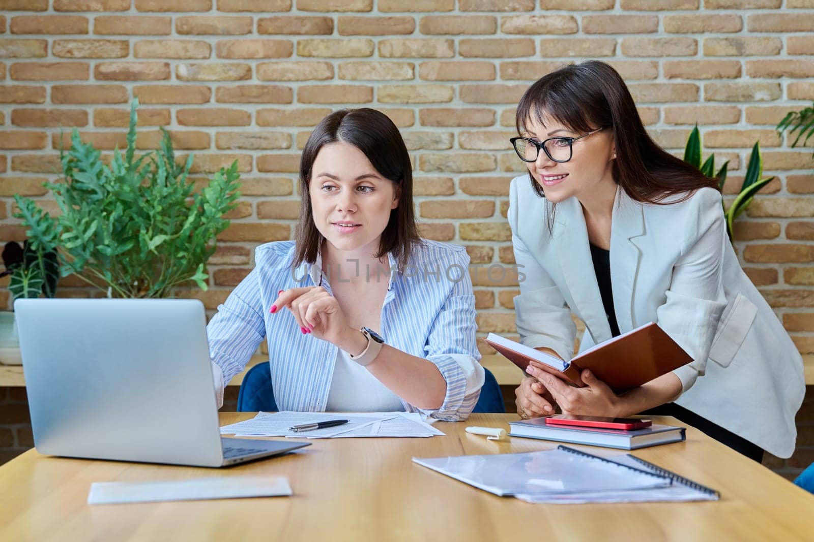 Two serious business women working in office, typing on laptop by VH-studio