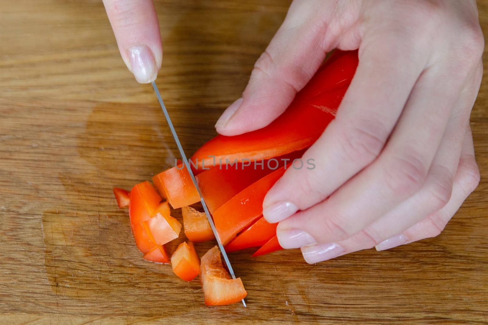 A woman's hand cuts red paprika into small slices close-up. The process of preparing salad from vegetables and fruits. High quality photo. by SERSOL