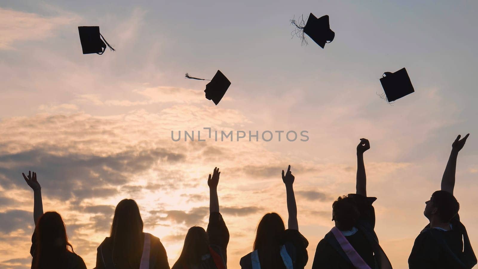 Student graduates toss their caps at sunset