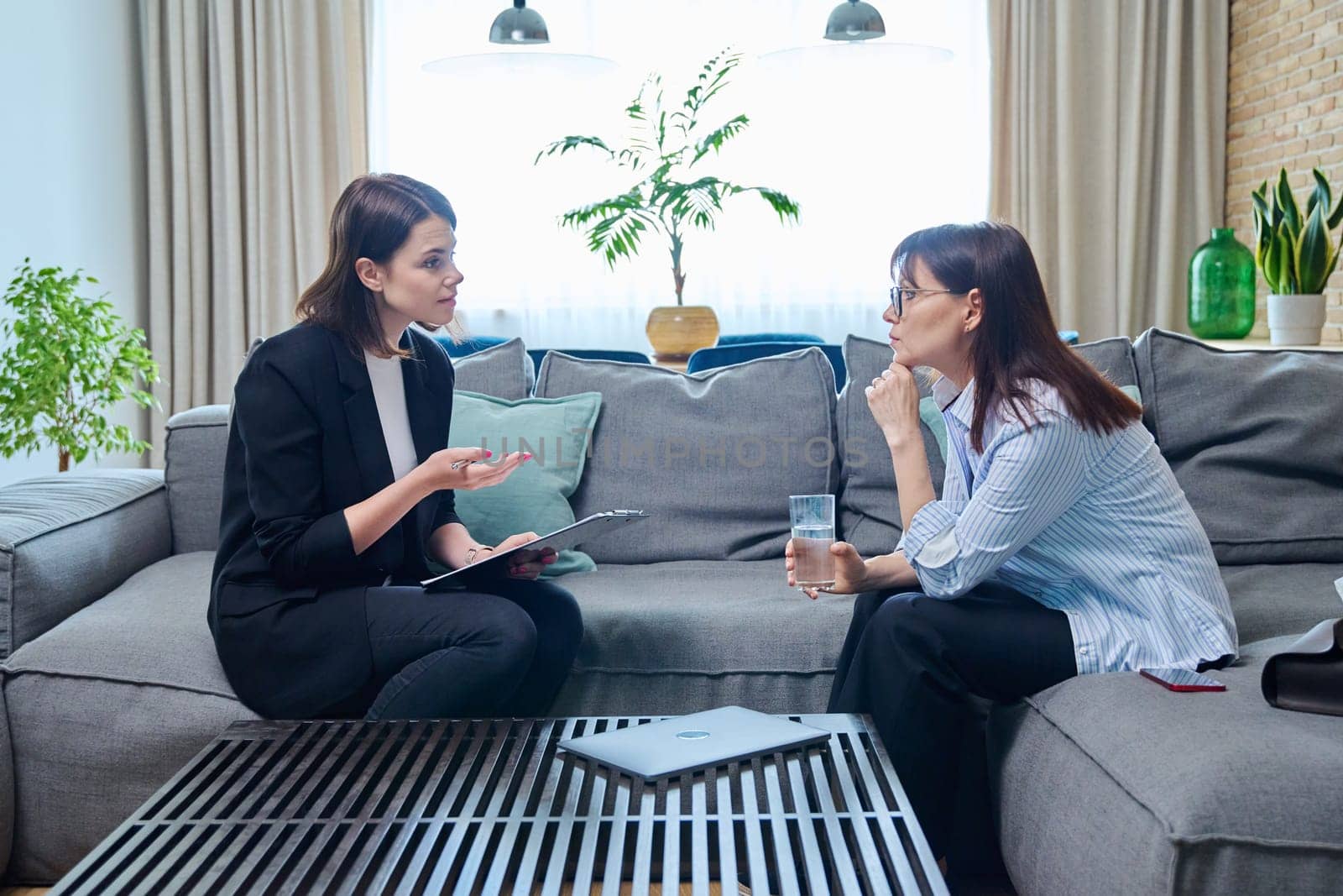 Middle-aged woman at meeting with psychologist counselor, sitting on couch in office. Mental problems of age female, psychological support help. Psychology psychotherapy therapy treatment healthcare