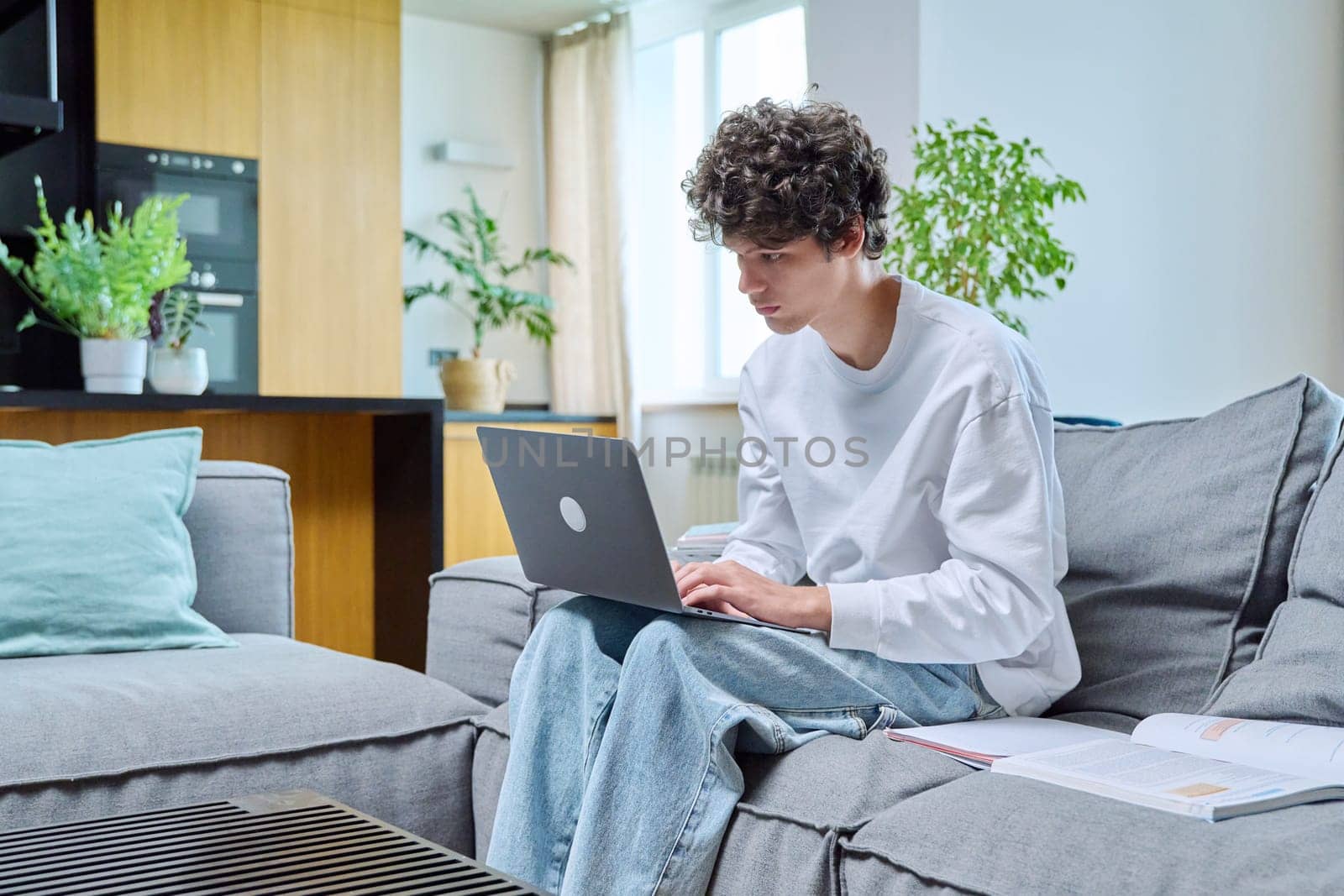 Handsome guy college student studying at home typing on laptop, sitting on sofa by VH-studio