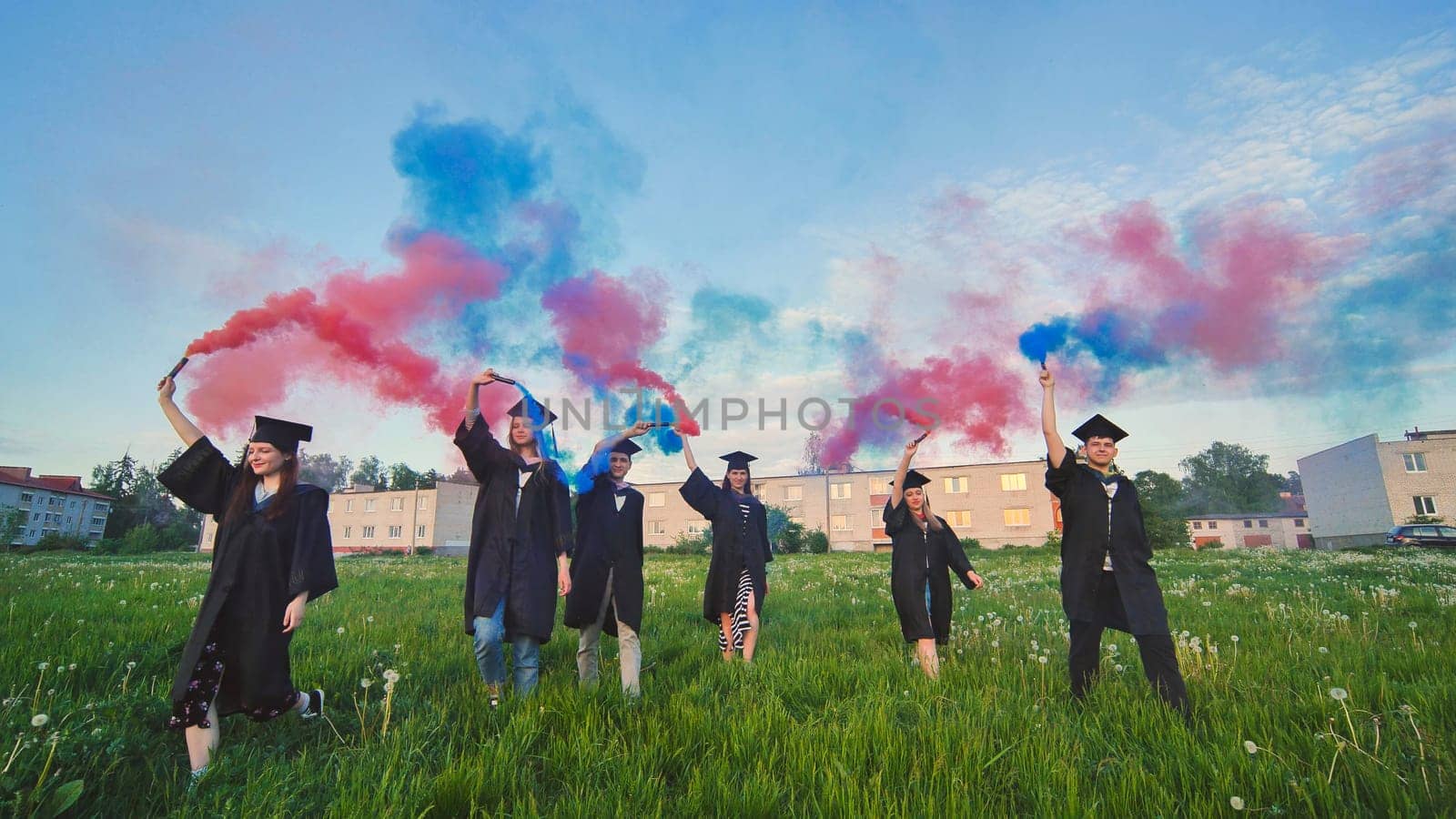 Graduates in costume walk with a smoky multi-colored smoke at sunset by DovidPro