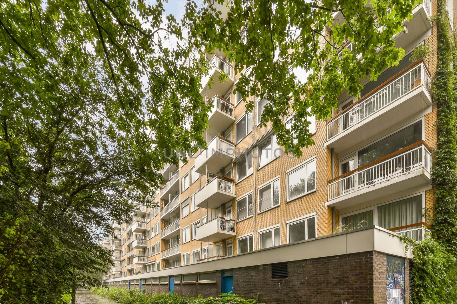 an apartment complex with trees and bushes in the foreground area on a sunny day, london, uk - stock photo