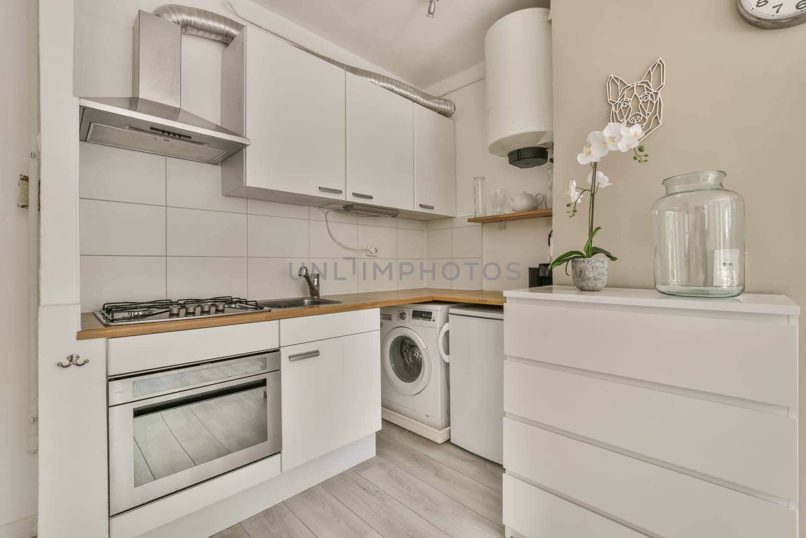 a small kitchen with white cupboards and wooden counter tops on the wall above it is a glass vase filled with flowers