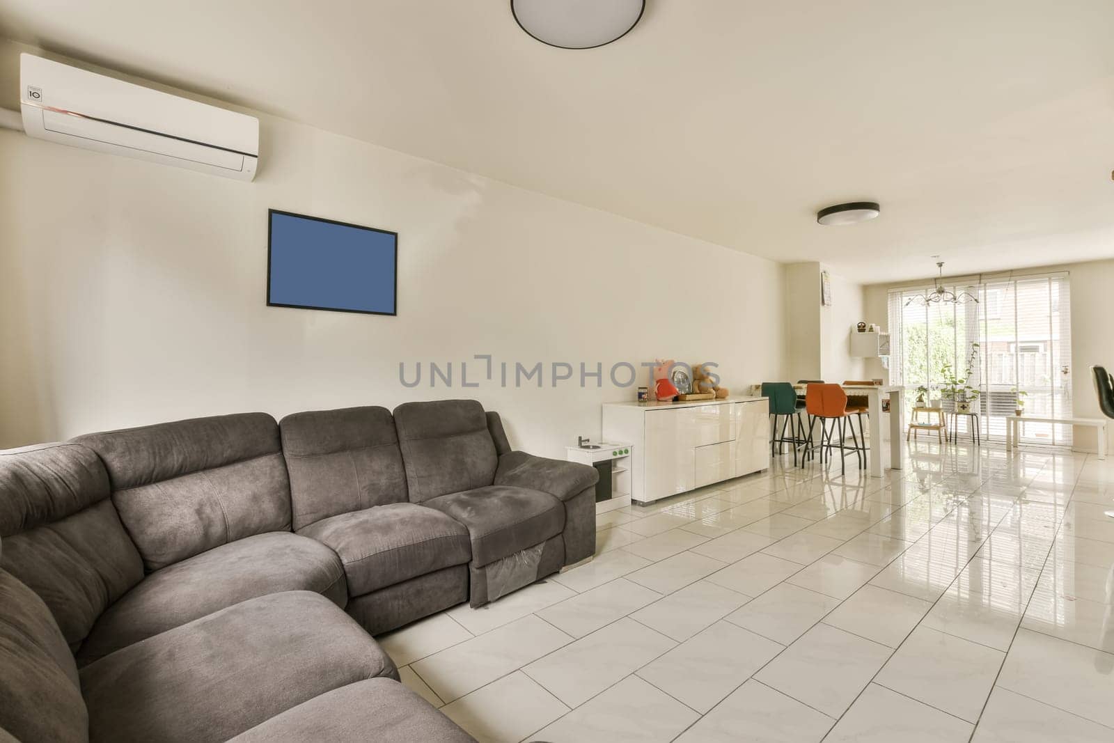 a living room with white tile flooring and an air condition heater on the wall in front of the couch