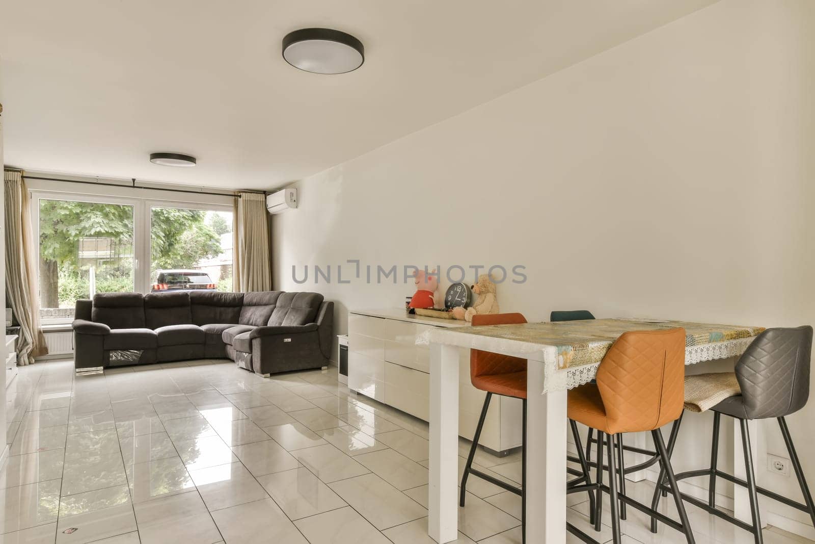 a living room and kitchen area in a house with white tile flooring, two bar stools and an open window