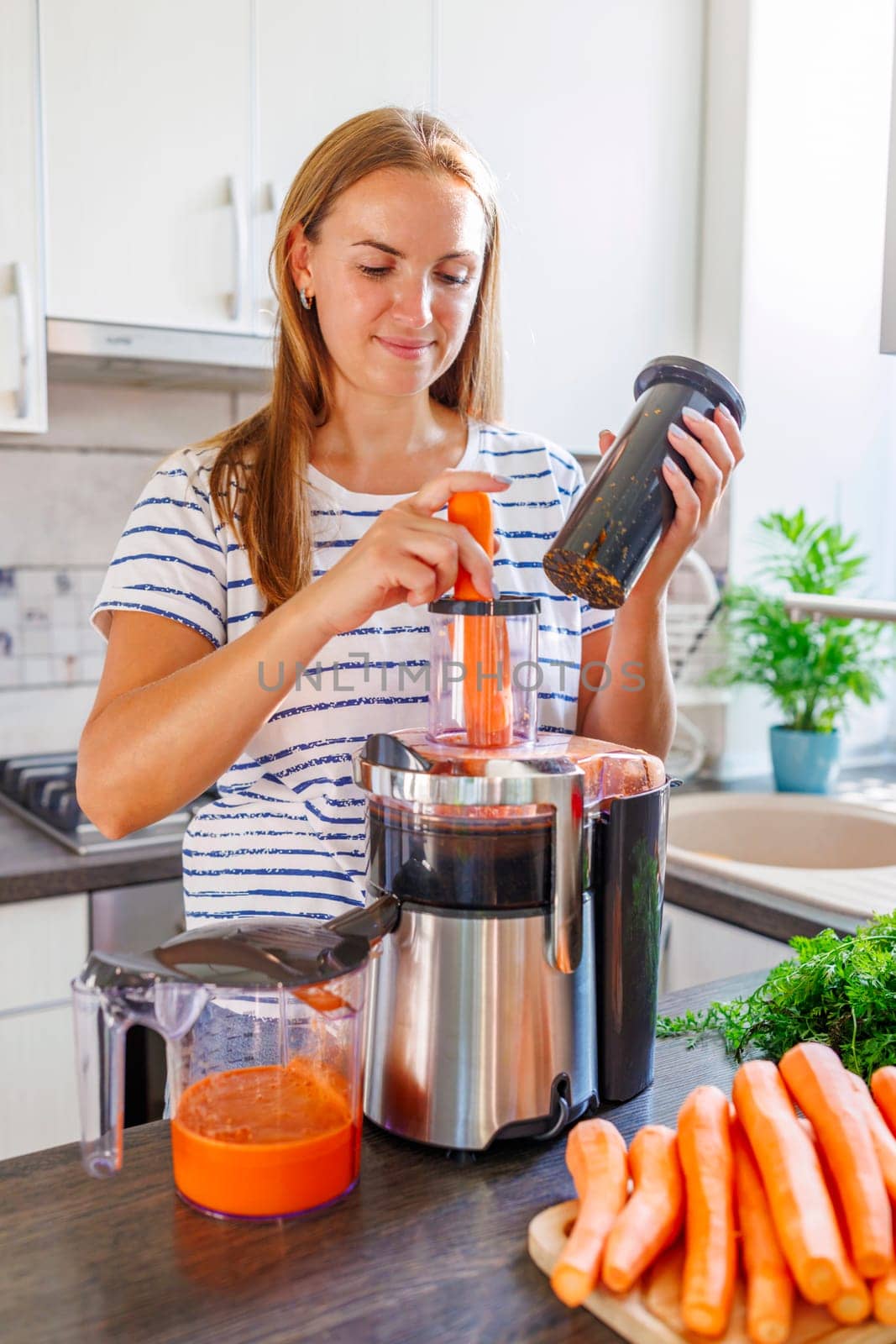 A woman making carrot juice from fresh carrots with a home juicer in the kitchen by andreyz