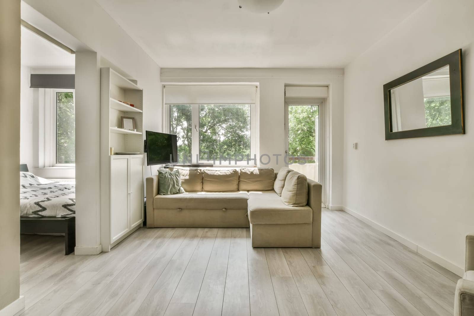 a living room with wood flooring and white walls in the background is a large window that looks out onto trees