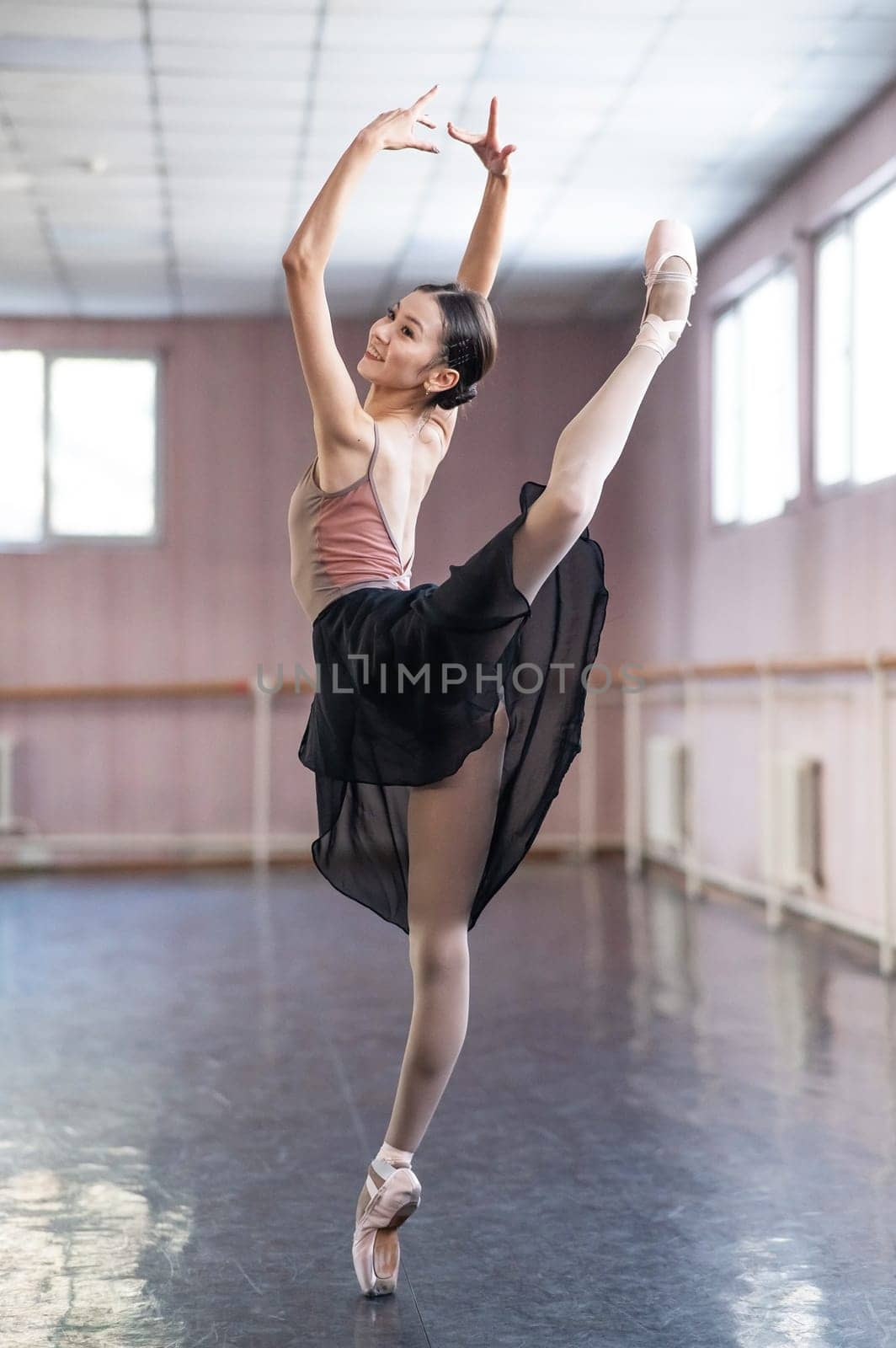 Graceful Asian ballerina in a beige bodysuit and black skirt is rehearsing in a dance class. by mrwed54