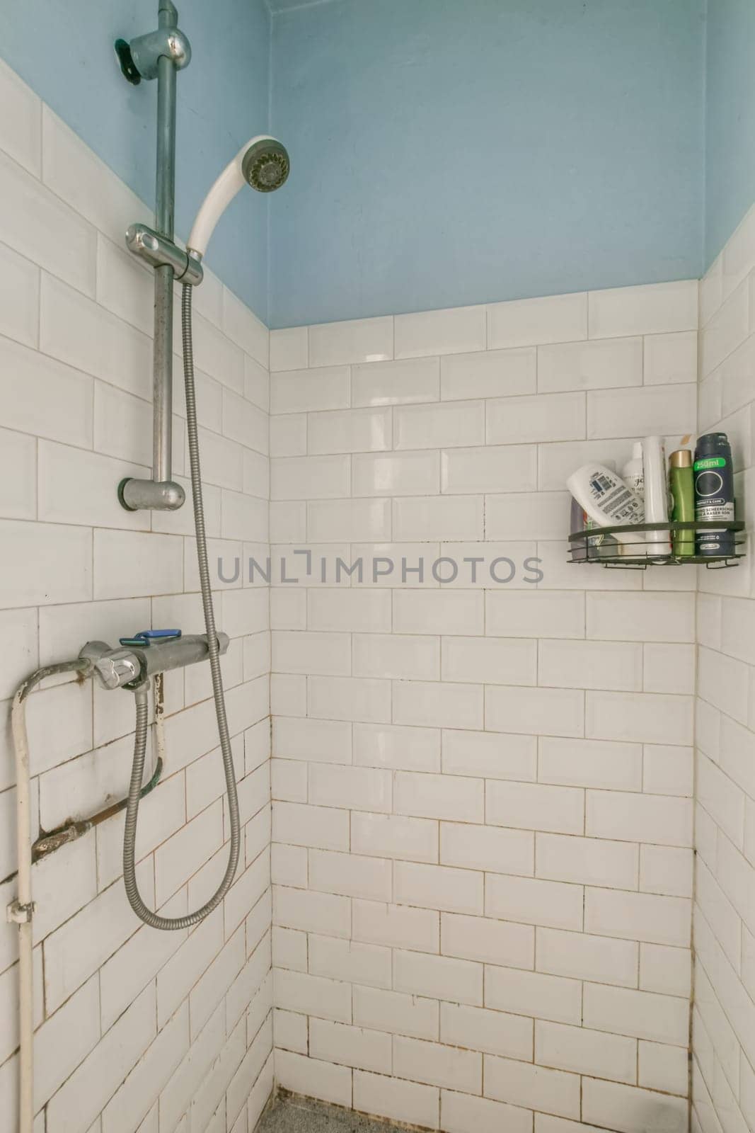 a bathroom with white tiles on the walls, and a shower head mounted to the wall next to the tub