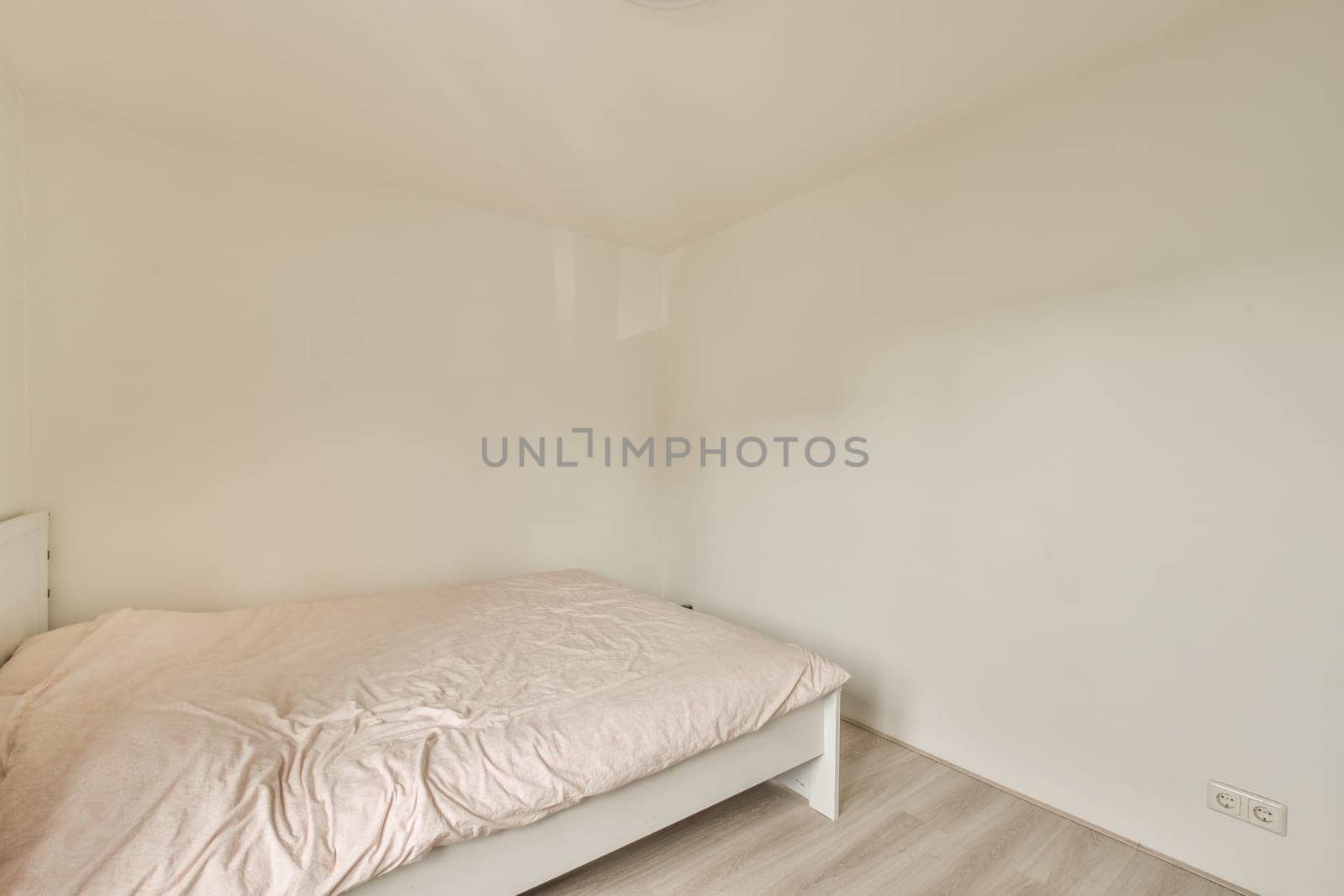 a bed in the corner of a room with white walls and wood flooring on the right side of the room