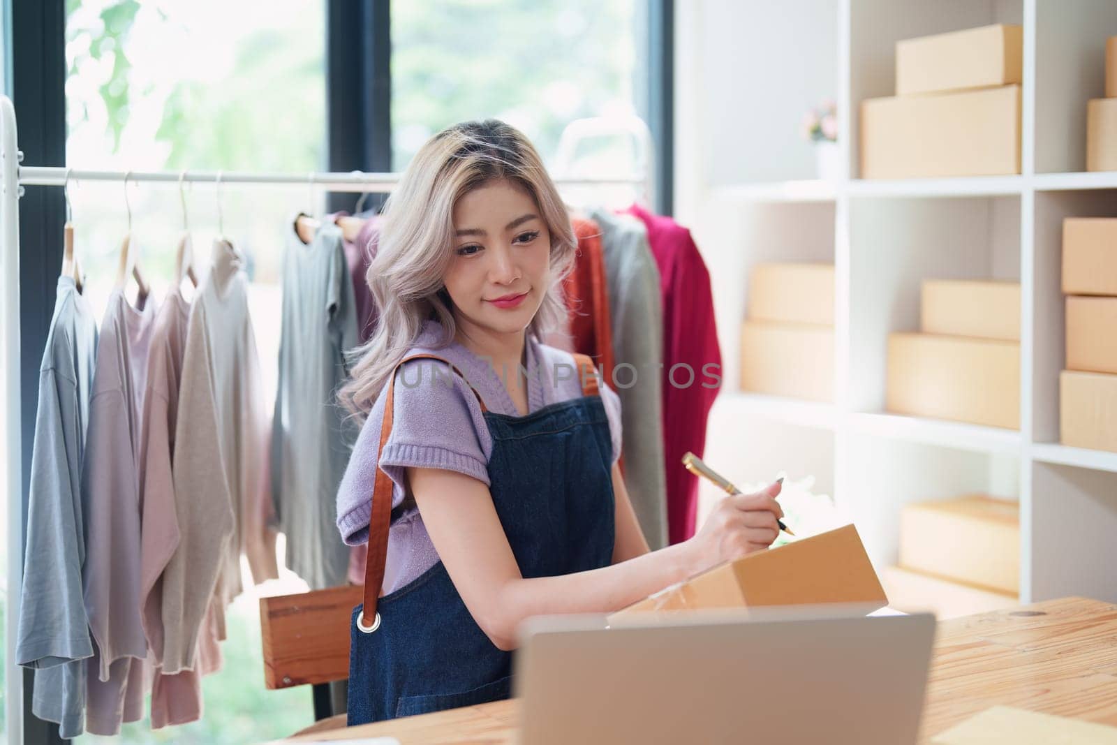 Starting small business entrepreneur of independent Asian female online seller talking on the phone with a customer and packing products for delivery to the customer. and SME delivery concept by Manastrong