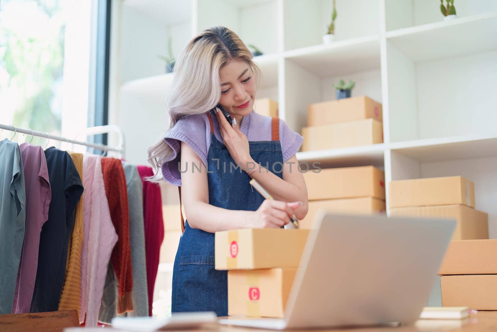 Starting small business entrepreneur of independent Asian female online seller talking on the phone with a customer and packing products for delivery to the customer. and SME delivery concept.