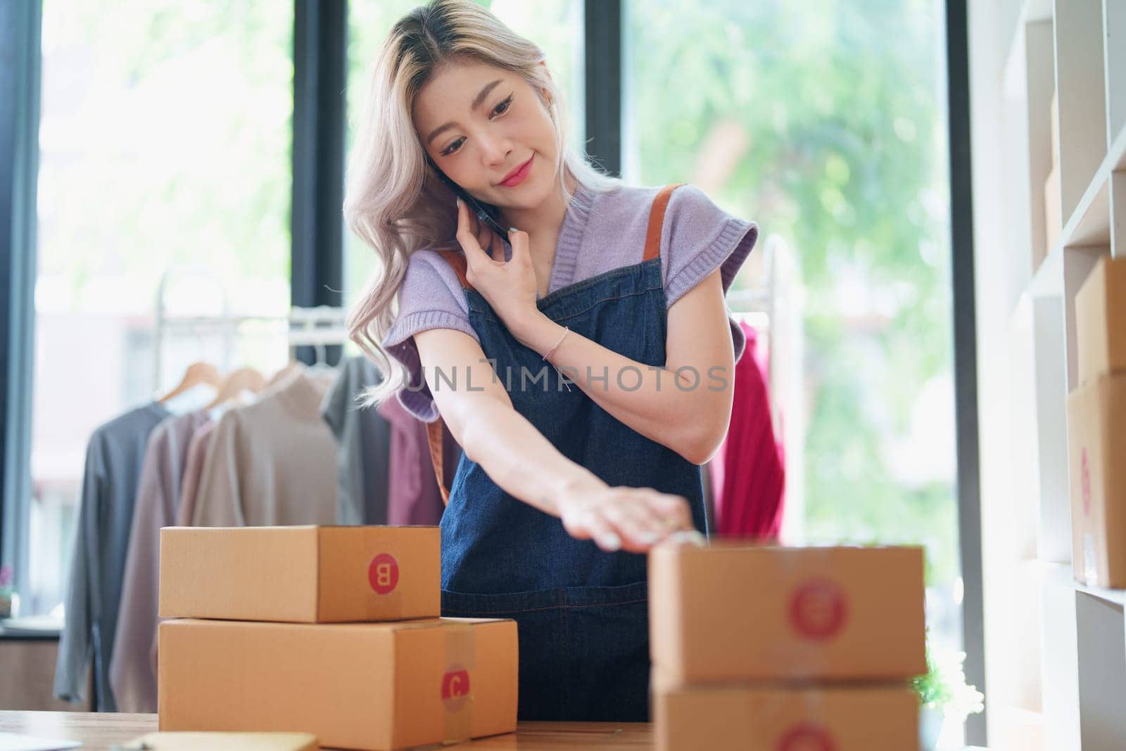 Starting small business entrepreneur of independent Asian female online seller talking on the phone with a customer and packing products for delivery to the customer. and SME delivery concept.