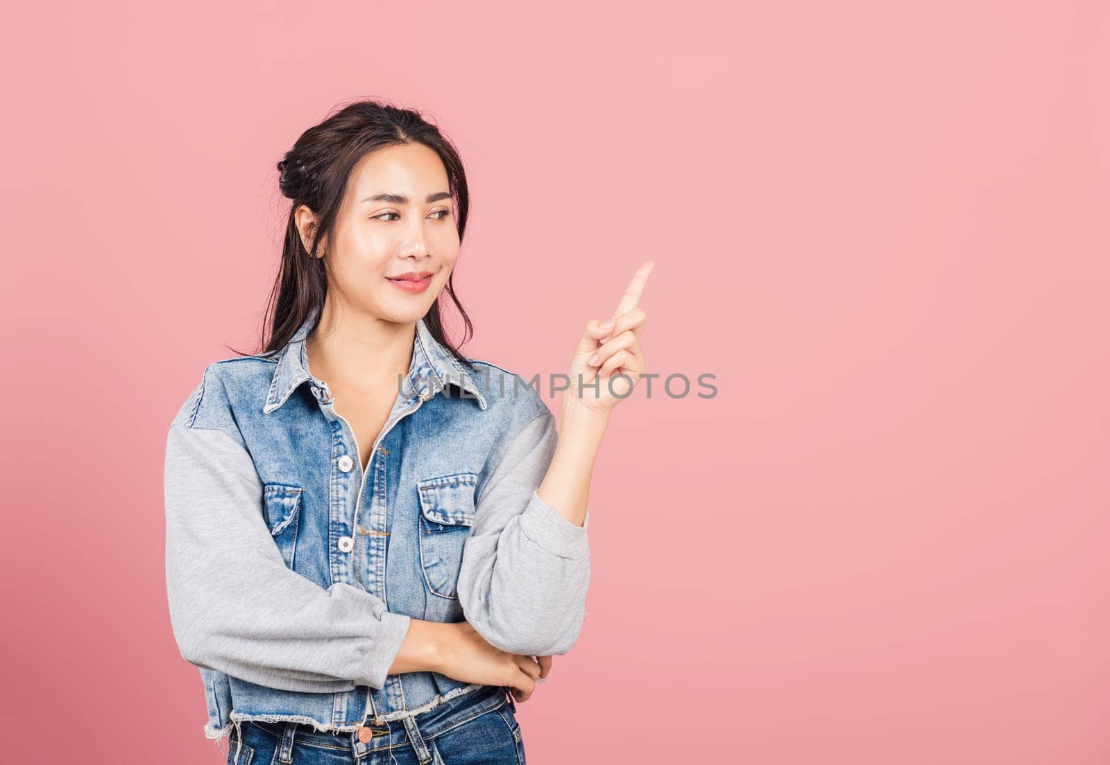 Happy Asian portrait beautiful cute young woman standing smiling indicate finger empty space looking to space, studio shot isolated on pink background, Thai female pointing index out with copy space