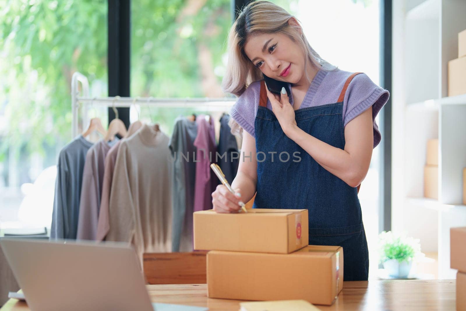 Starting small business entrepreneur of independent Asian female online seller talking on the phone with a customer and packing products for delivery to the customer. and SME delivery concept by Manastrong