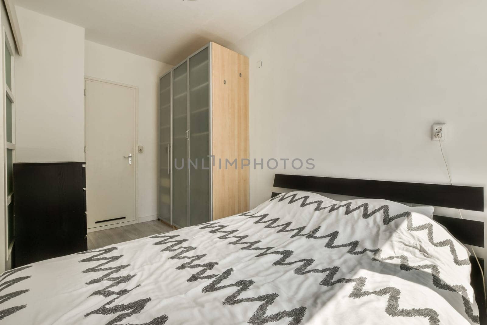 a bedroom with a bed, dresser and mirror on the wall in front of the bed is black and white