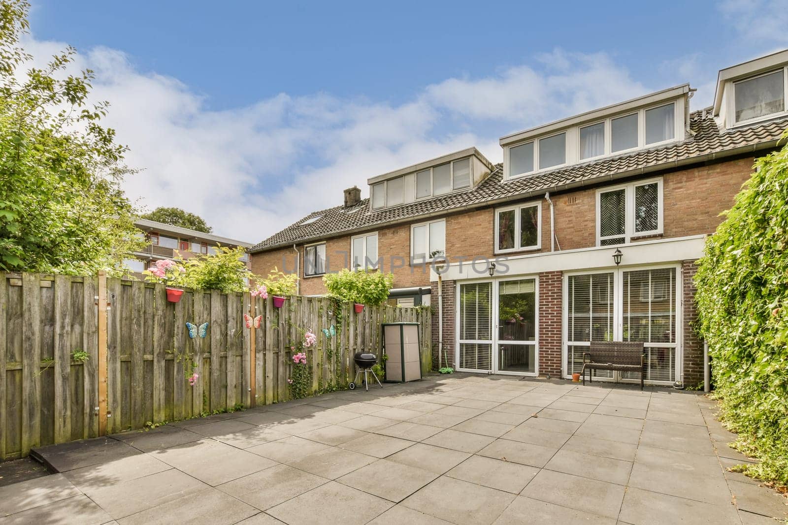 a backyard area with a wooden fence and green plants on the side of the house there is a blue sky in the background