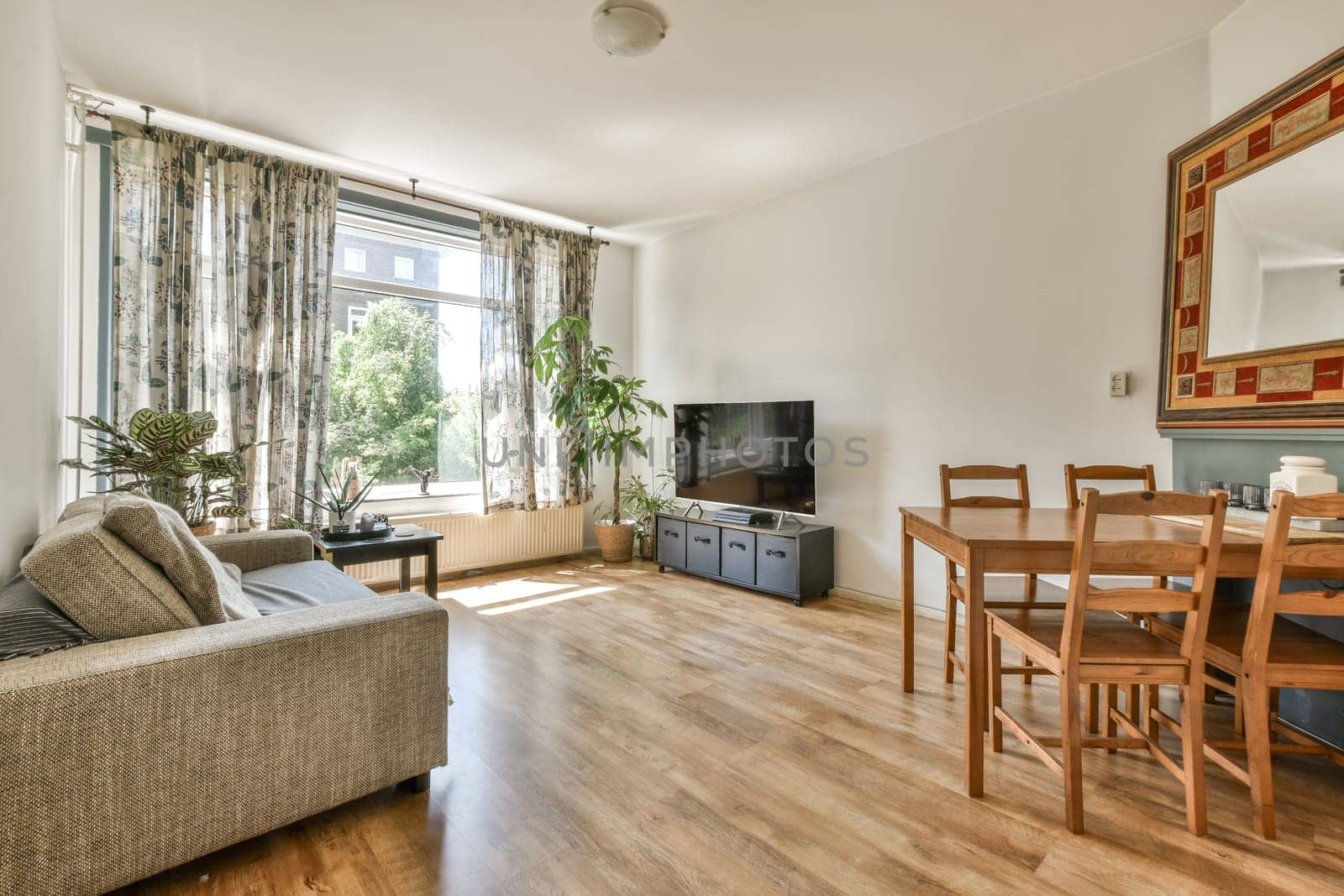 a living room with wood flooring and a large mirror on the wall above the couch is a small dining table