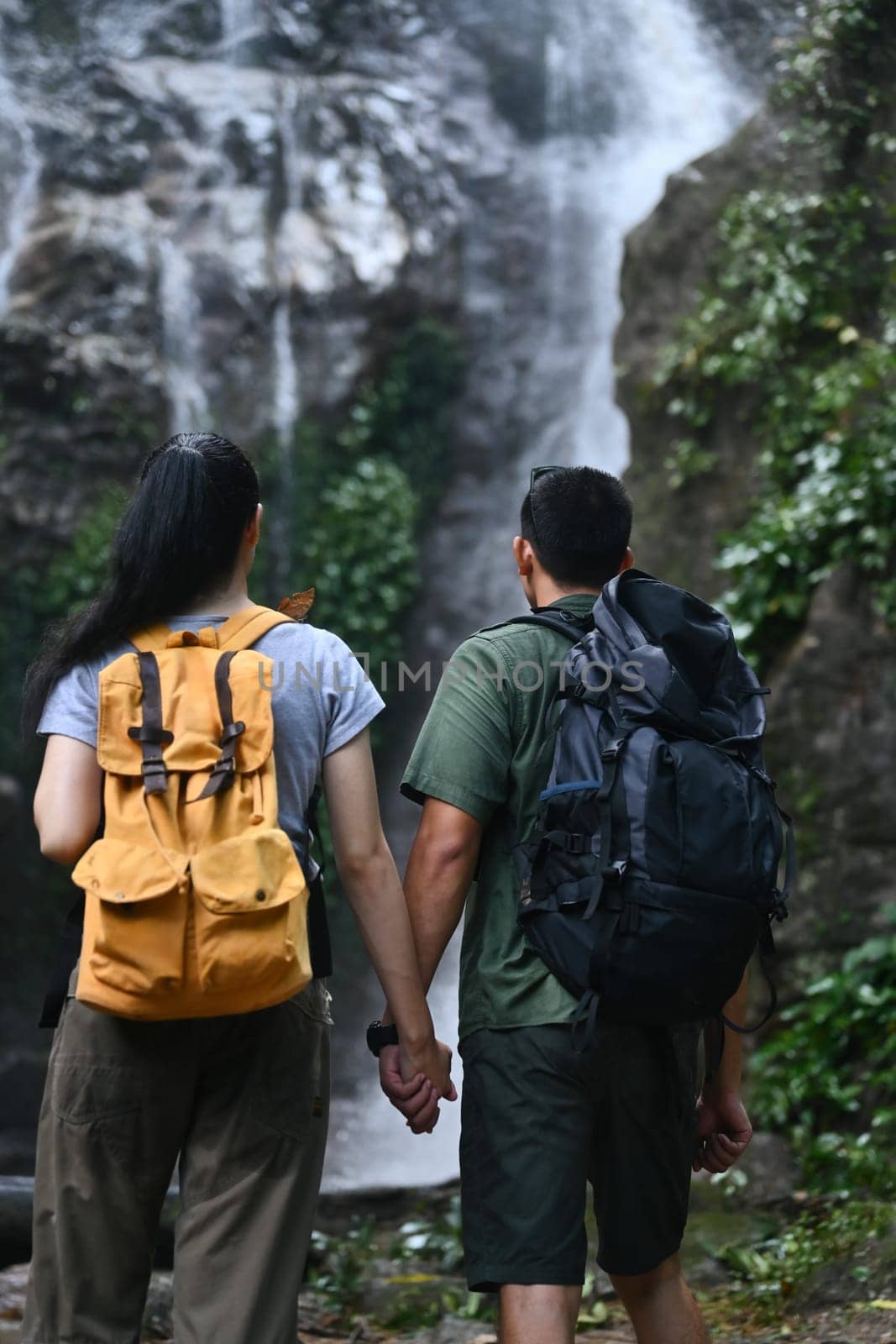 Rear view of loving couple tourist with backpack admiring a beautiful waterfall.