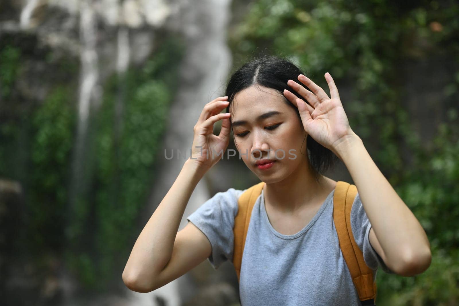 Tired female tourist wiping sweat on forehead during hiking in forest. Traveling, trekking and adventure concept.